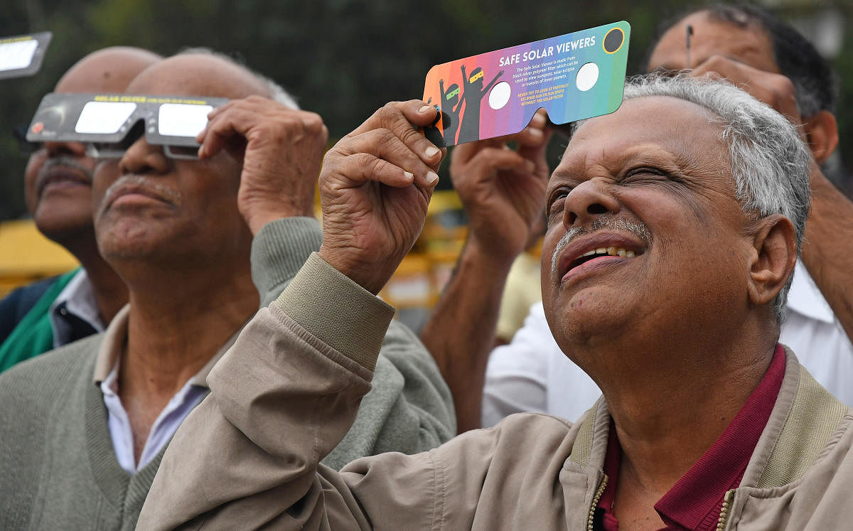 People try to get a glimpse of the solar eclipse from Town Hall, Bengaluru on Thursday. | DH Photo: Pushkar V