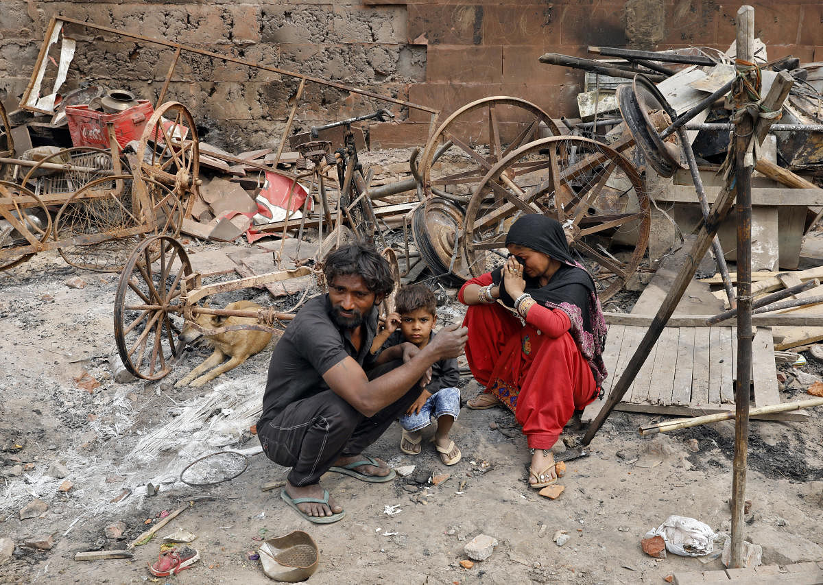 A woman sitting with her husband and their child next to damaged property after their house was burnt by a mob. REUTERS
