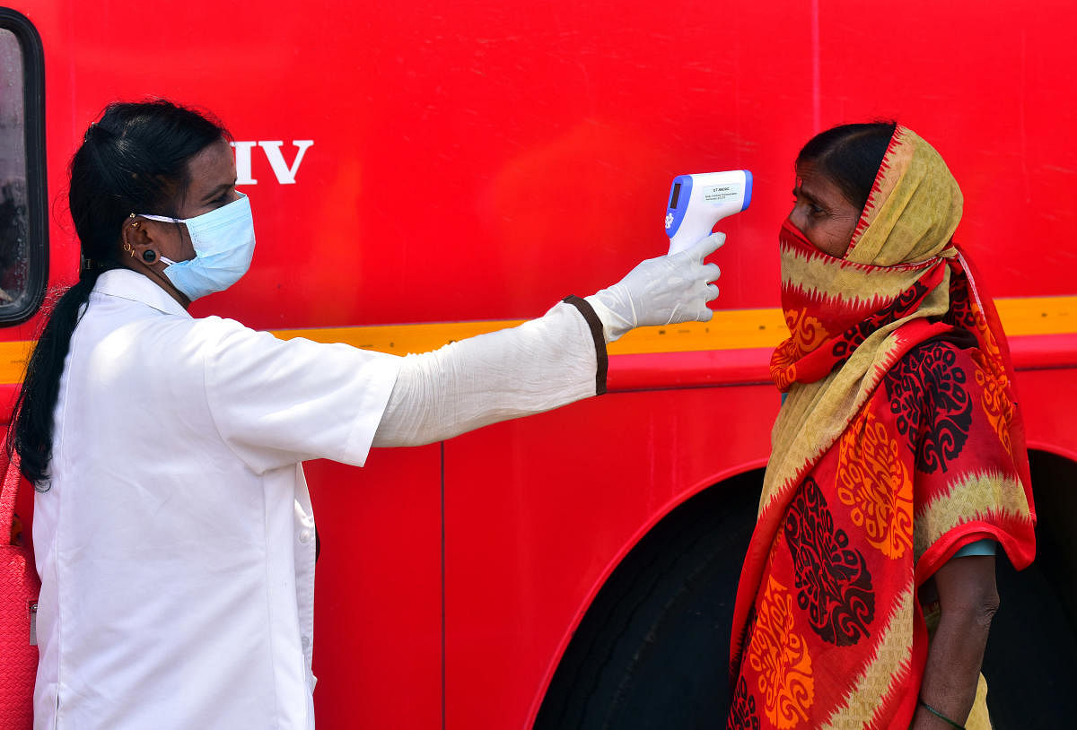 A health worker reads the temperature of a migrant woman, who came to board a KSRTC bus to reach her home town. DH photo/Anup Ragh T