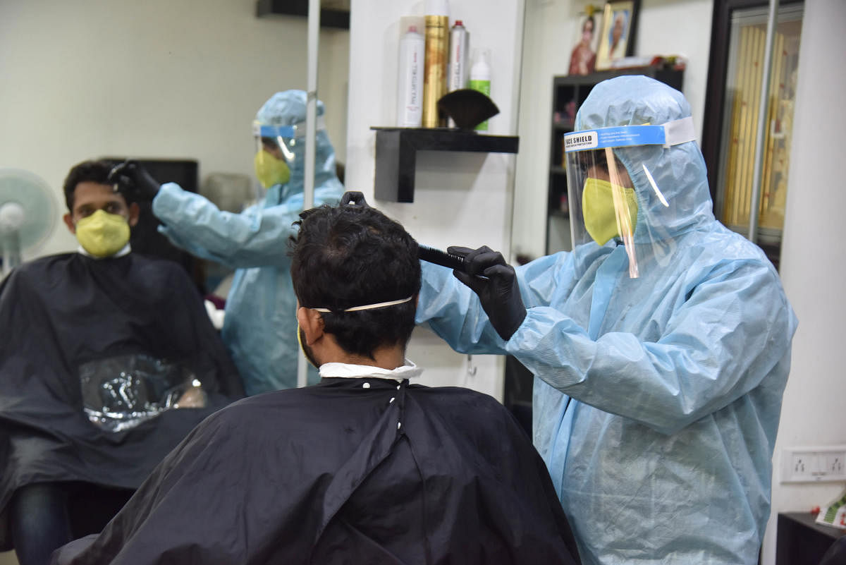 A hairstylist dons a PPE suit while attending to his customer at a salon at Kumara Krupa Road. DH Photo/Janardhan B K