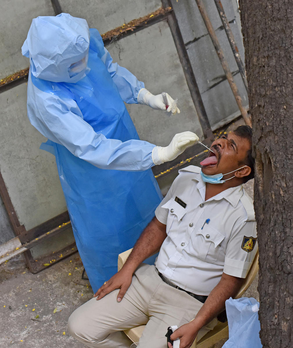 A healthcare worker takes the swab samples of a cop on Wednesday. (R) The Lokayukta officer was fumigated after a constable tested positive. DH PHOTO/S K DINESH & M S MANJUNATH