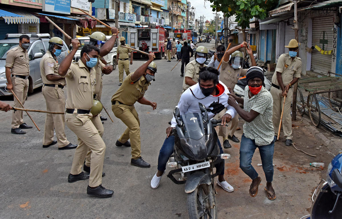 Cops cane two men riding a motorcyclist during the curfew in DJ Halli. DH PHOTO/M S MANJUNATH