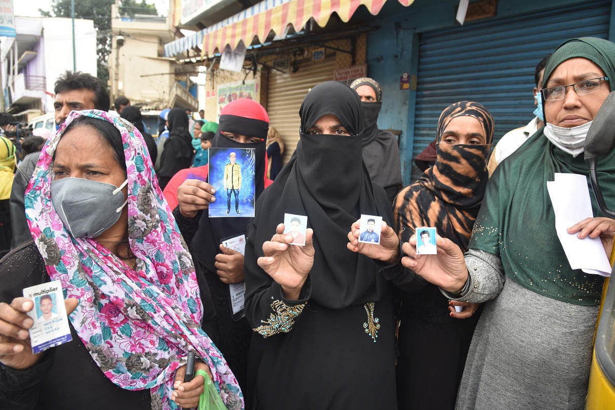 Women show the pictures of their male relatives who they said were arbitrarily picked up by the police in DJ Halli Bengaluru on Friday. DH PHOTO/S K DINESH