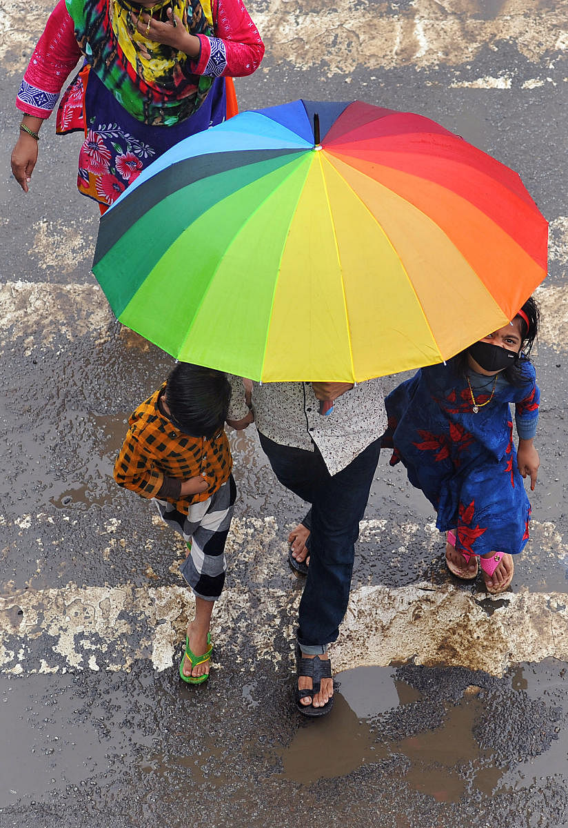 A man and two children take shelter under an umbrella on a Bengaluru street on Thursday. DH PHOTO/PUSHKAR V