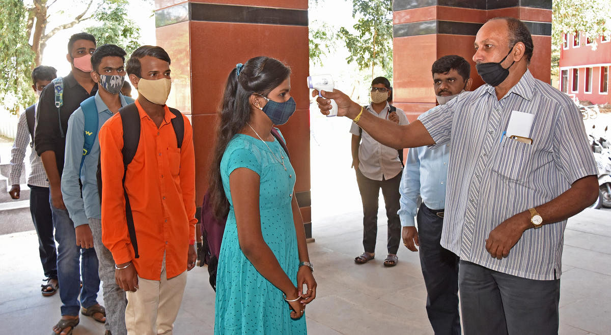 A staffer checks the temperature of students at Government Arts and Management College in Bengaluru. DH photo/M S Manjunath