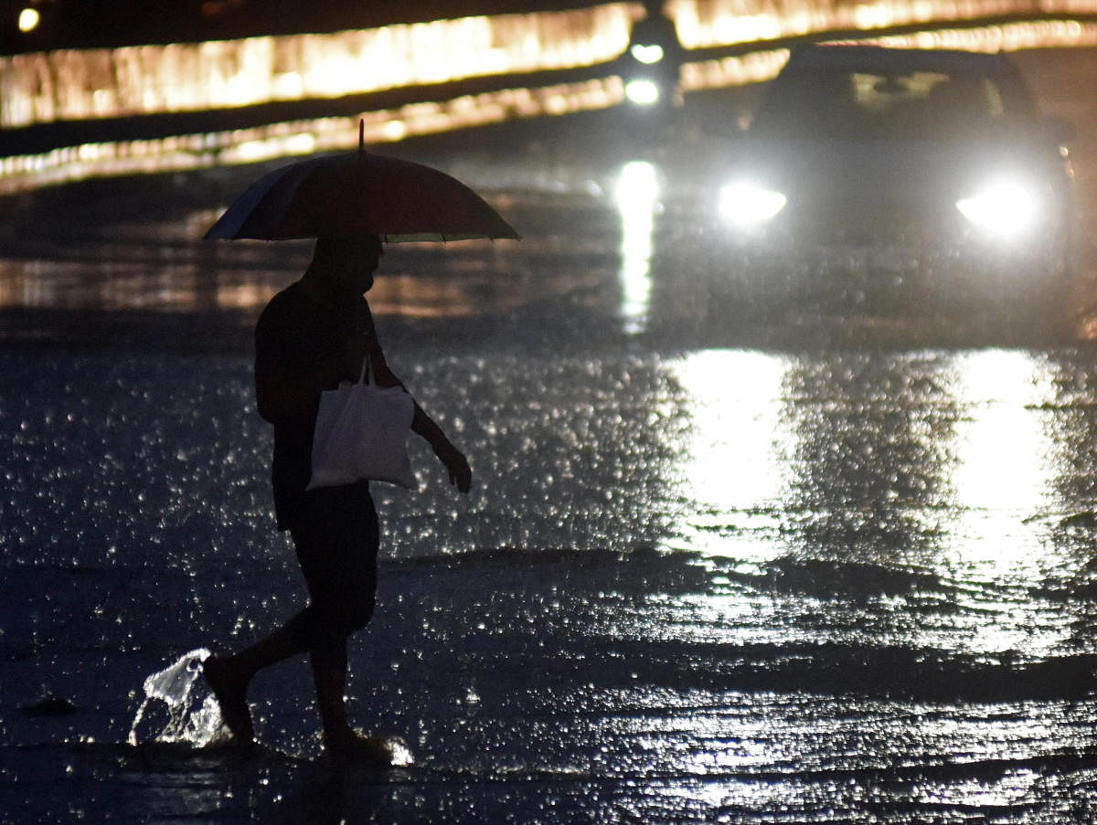 A man with an umbrella walks amid light vehicular traffic on a rain-filled Mysuru Road, Bengaluru, on Wednesday evening. DH PHOTO/ANUP RAGH T 
