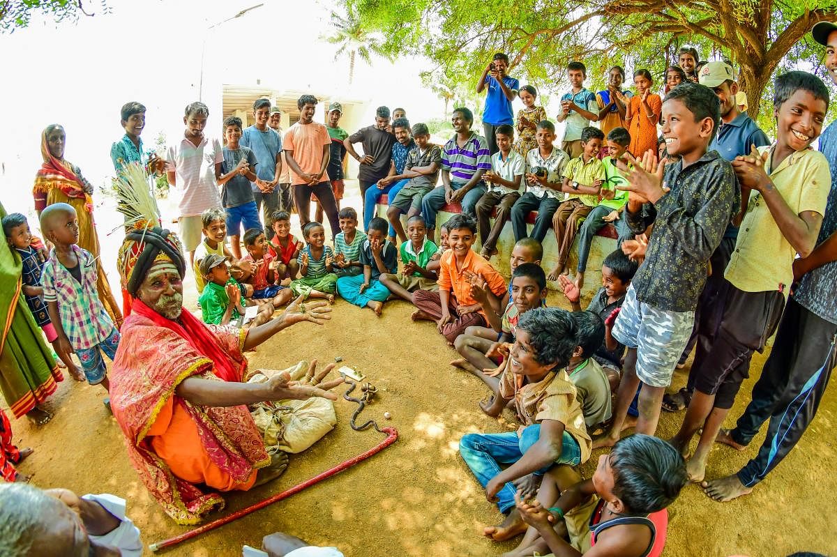 People, especially children, watch a Sudagaadu Sidda performing a trick.