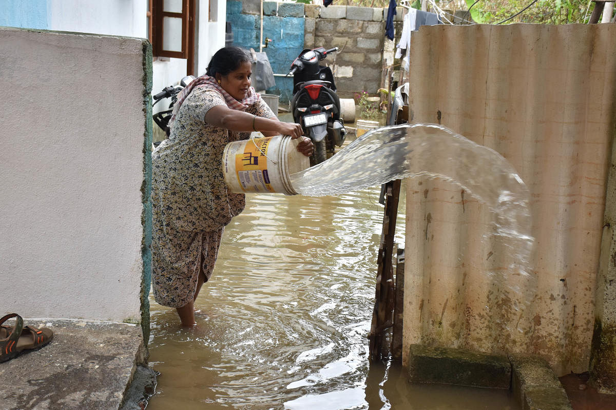 A woman drains rainwater from inside her house at Kodigehalli. DH Photo/B K Janardhan