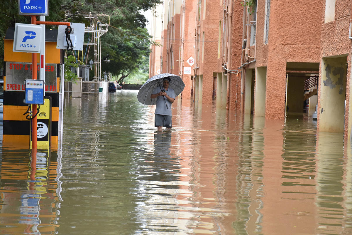A man with an umbrella walks in knee-deep water at the Kendriya Vihar apartment, North Bengaluru, on Friday. DH PHOTO/B K JANARDHAN