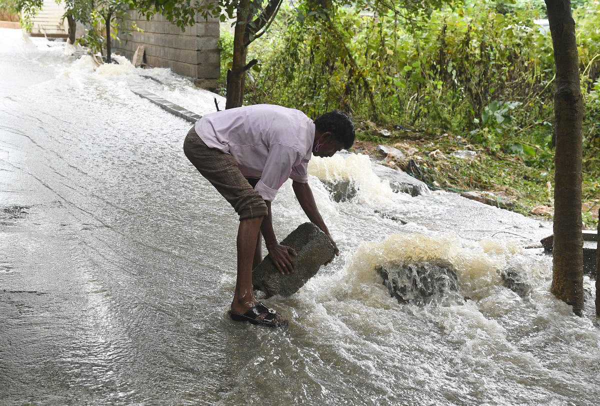 A man tries to divert the floodwater in Shettihalli, T Dasarahalli, after Shettihalli Lake breached following heavy rains on Friday. DH PHOTO/B H SHIVAKUMAR