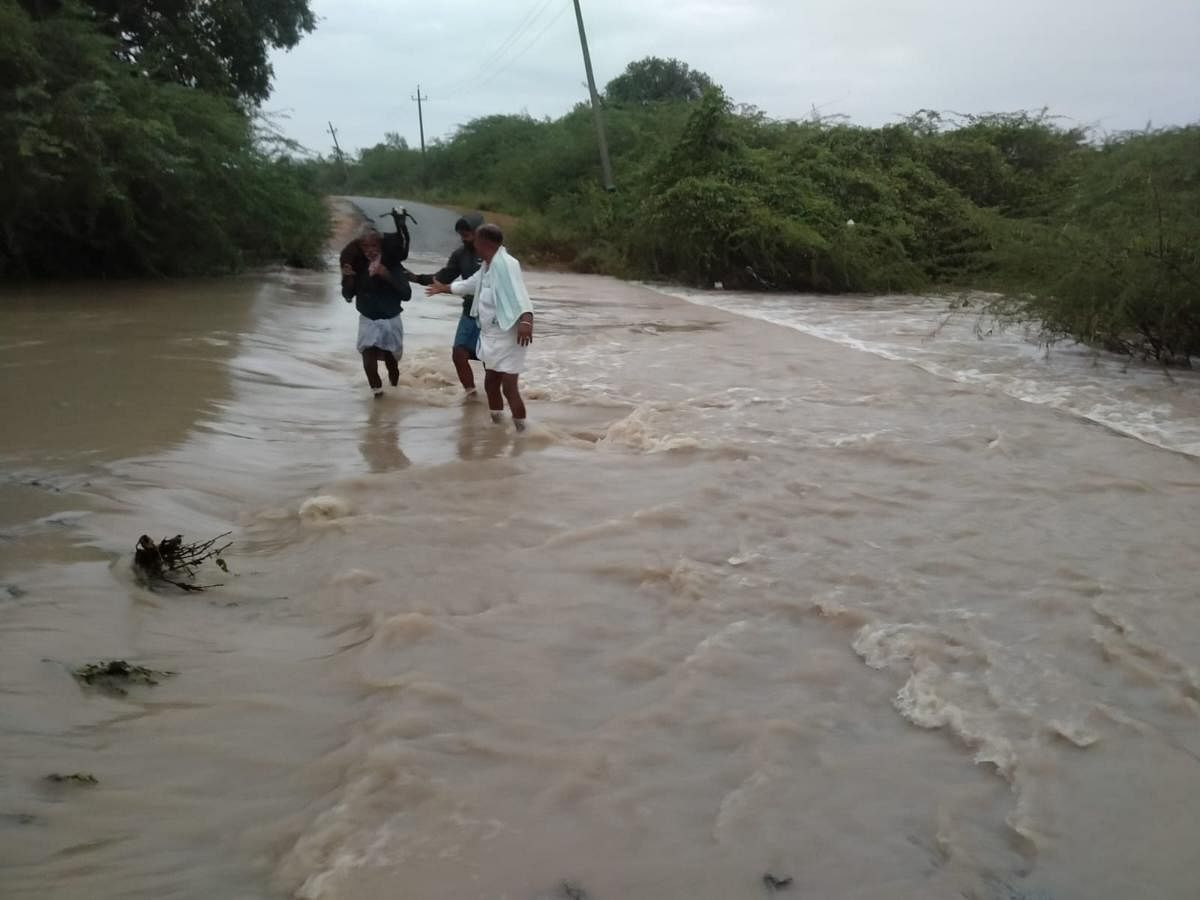 Residents wade through a flooded road in Maski taluk of Raichur district. Credit: DH Photo