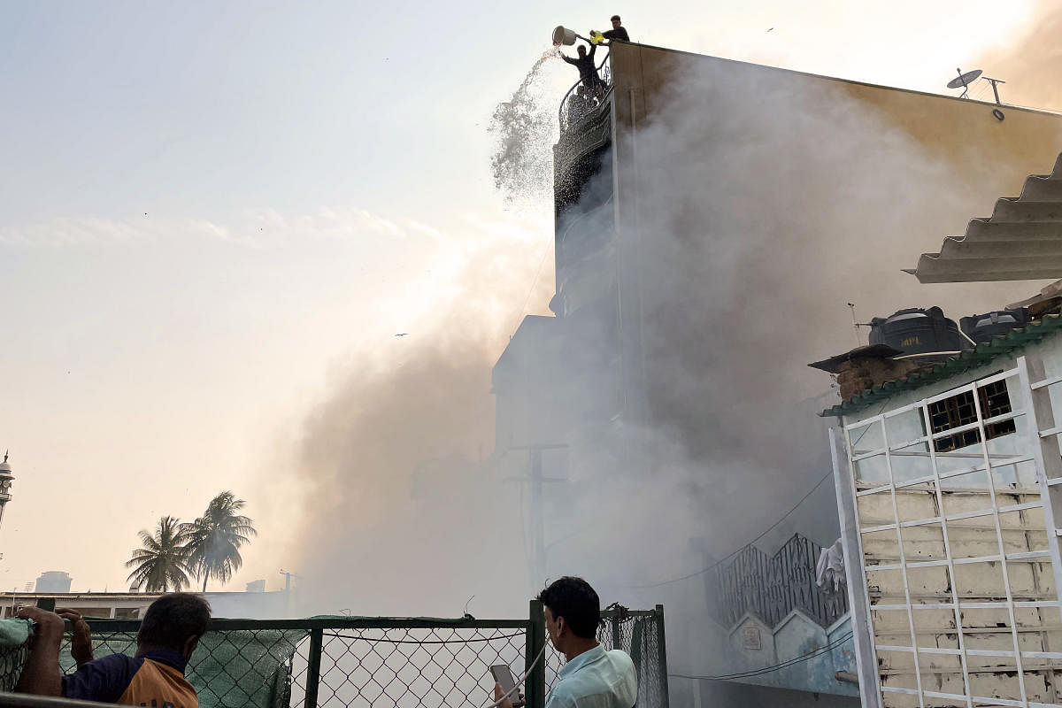 Two residents pour buckets of water on the fire scene from atop a building at Bamboo Bazaar, Shivajinagar, on Saturday. Credit: DH Photo/Pushkar V