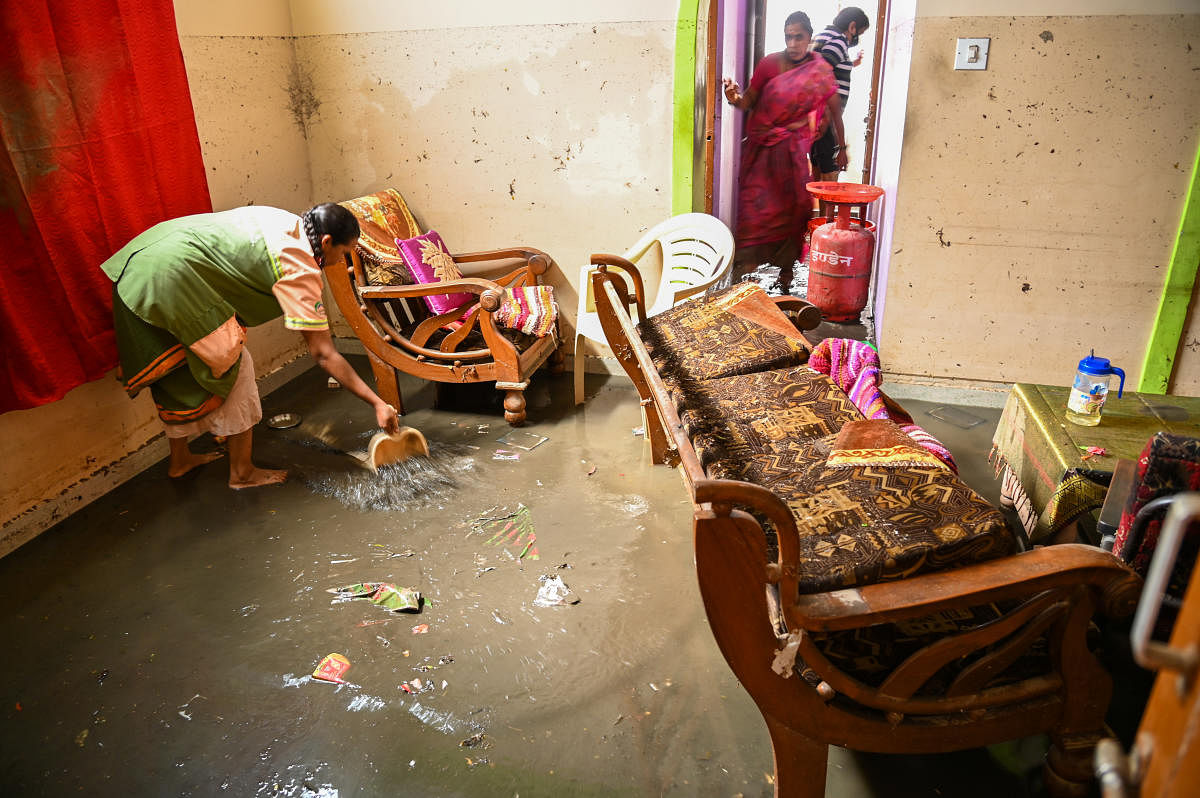 Civic workers join hands with the occupants of a flooded house in removing the sewage water from a clogged drain which inundated many houses in Kamakya Layout in the city. Credit: DH Photo