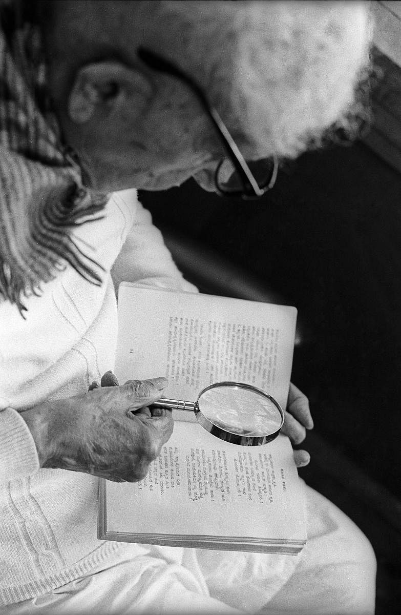 Kuvempu uses a magnifying glass to read Kannada poetry.