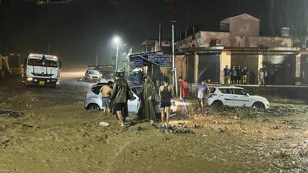 <div class="paragraphs"><p>SDRF personnel stand near two vehicles stuck in a manhole amid heavy rains, in Rishikesh.</p></div>