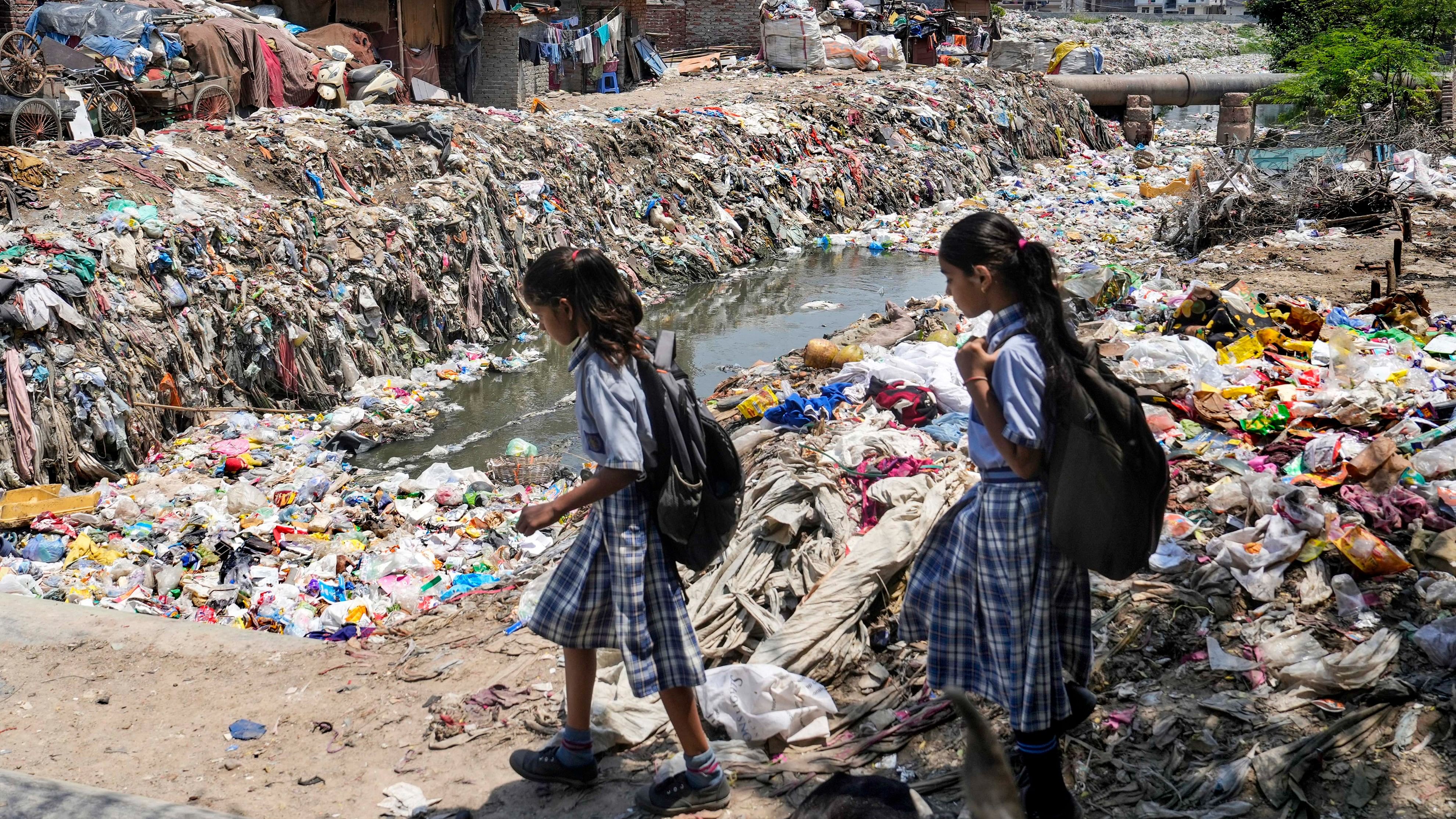 <div class="paragraphs"><p>School children walk past a semi-dry drain choked with garbage at Taimoor Nagar.&nbsp;</p></div>