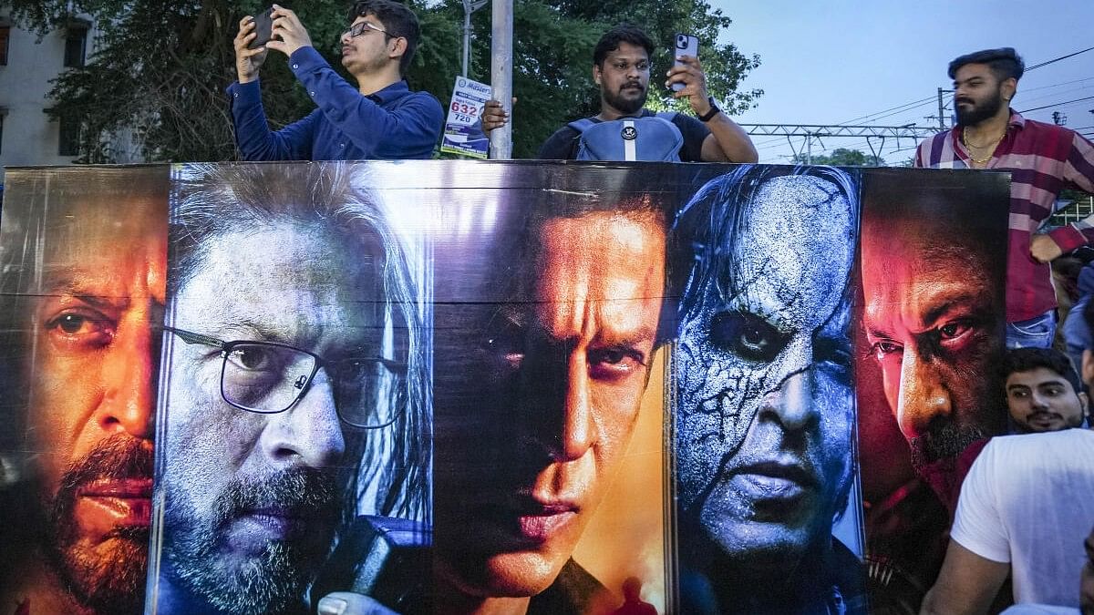 <div class="paragraphs"><p>Fans wait near a poster of Bollywood actor Shah Rukh Khan outside a cinema hall to watch the screening of his latest film 'Jawan'.</p></div>