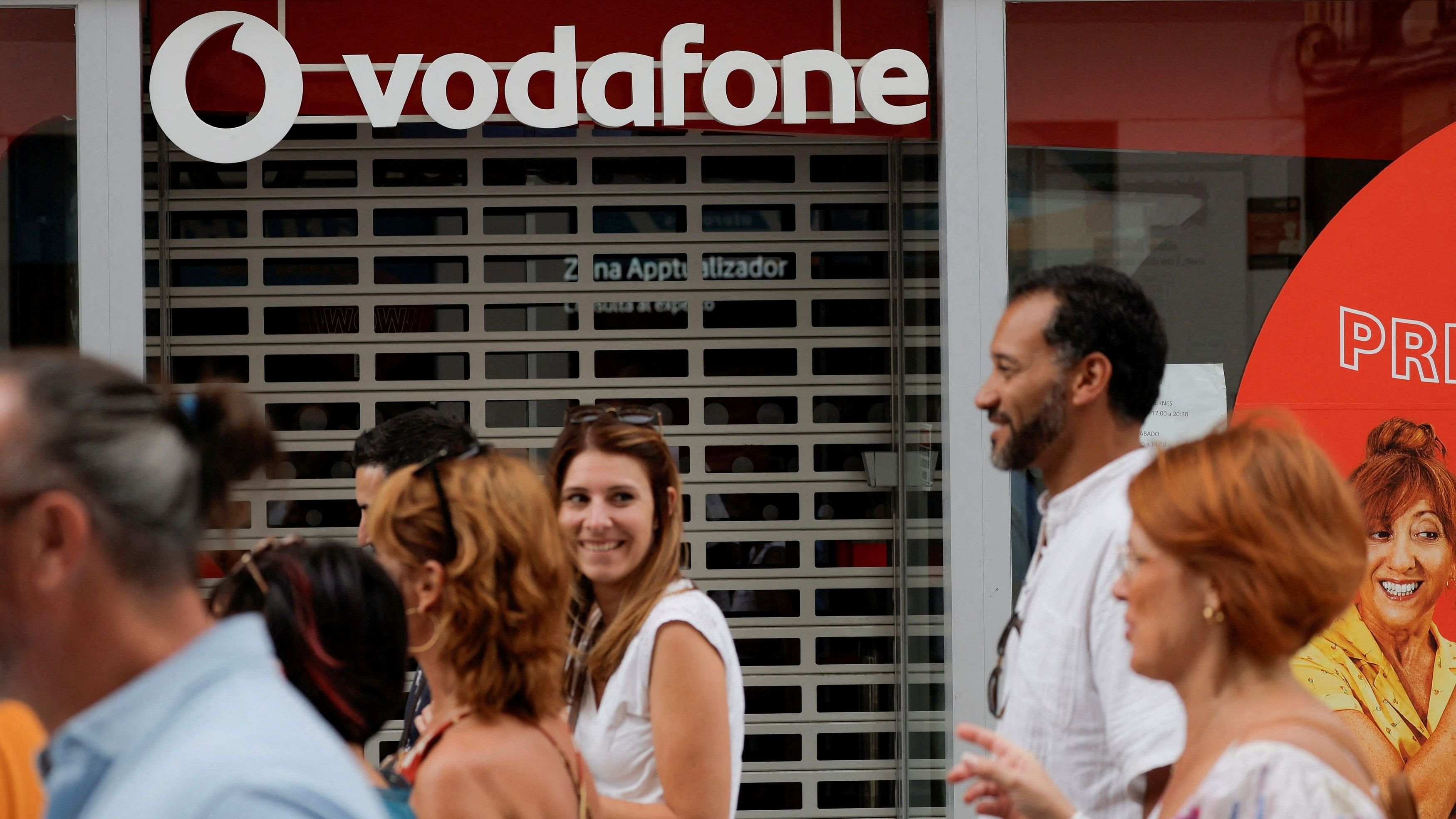 <div class="paragraphs"><p>People walk past a Vodafone store in Ronda, Spain.</p></div>