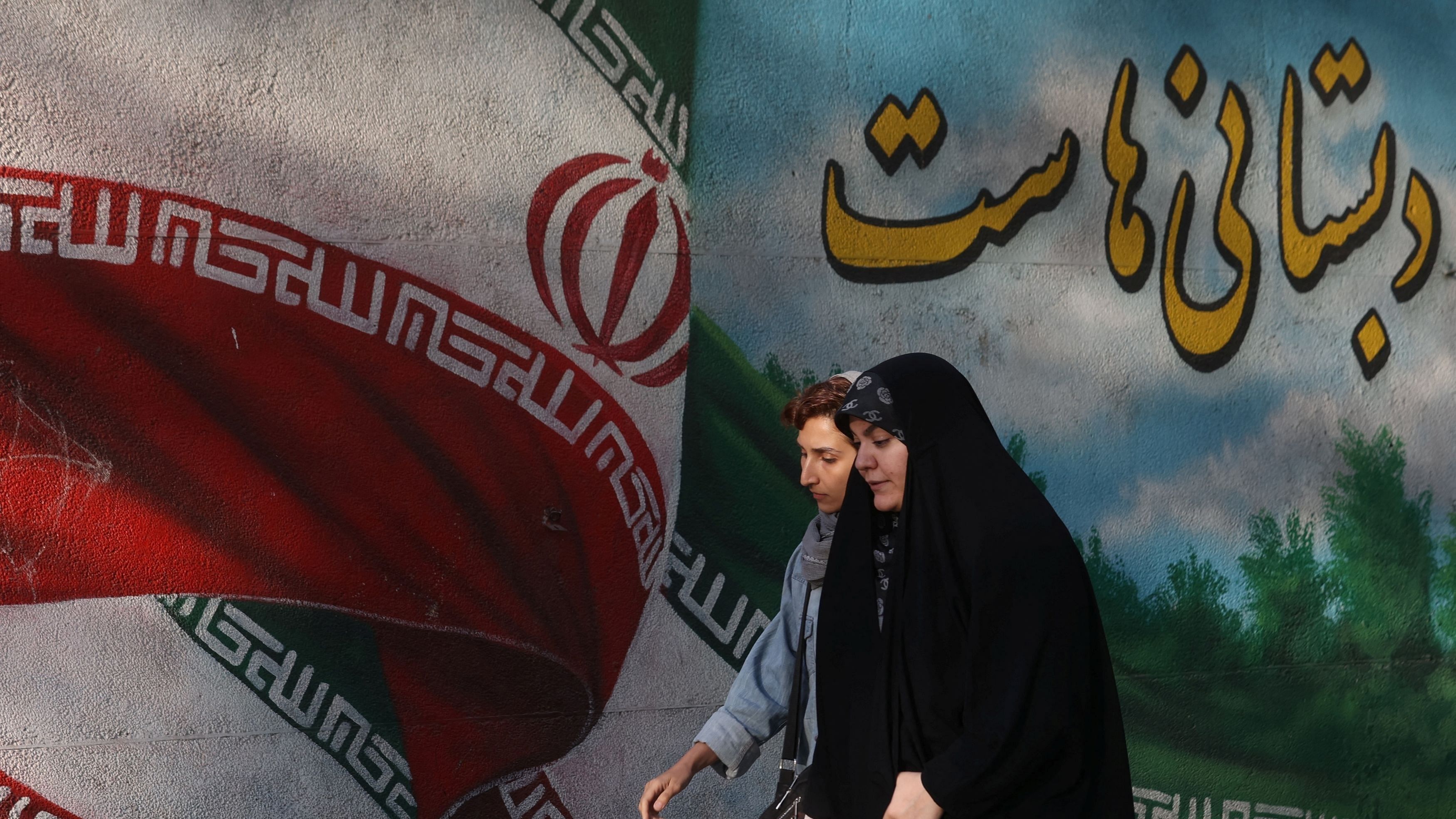 <div class="paragraphs"><p>Iranian women walks past a mural with a picture of the Iranian flag on a street in Tehran, Iran</p></div>