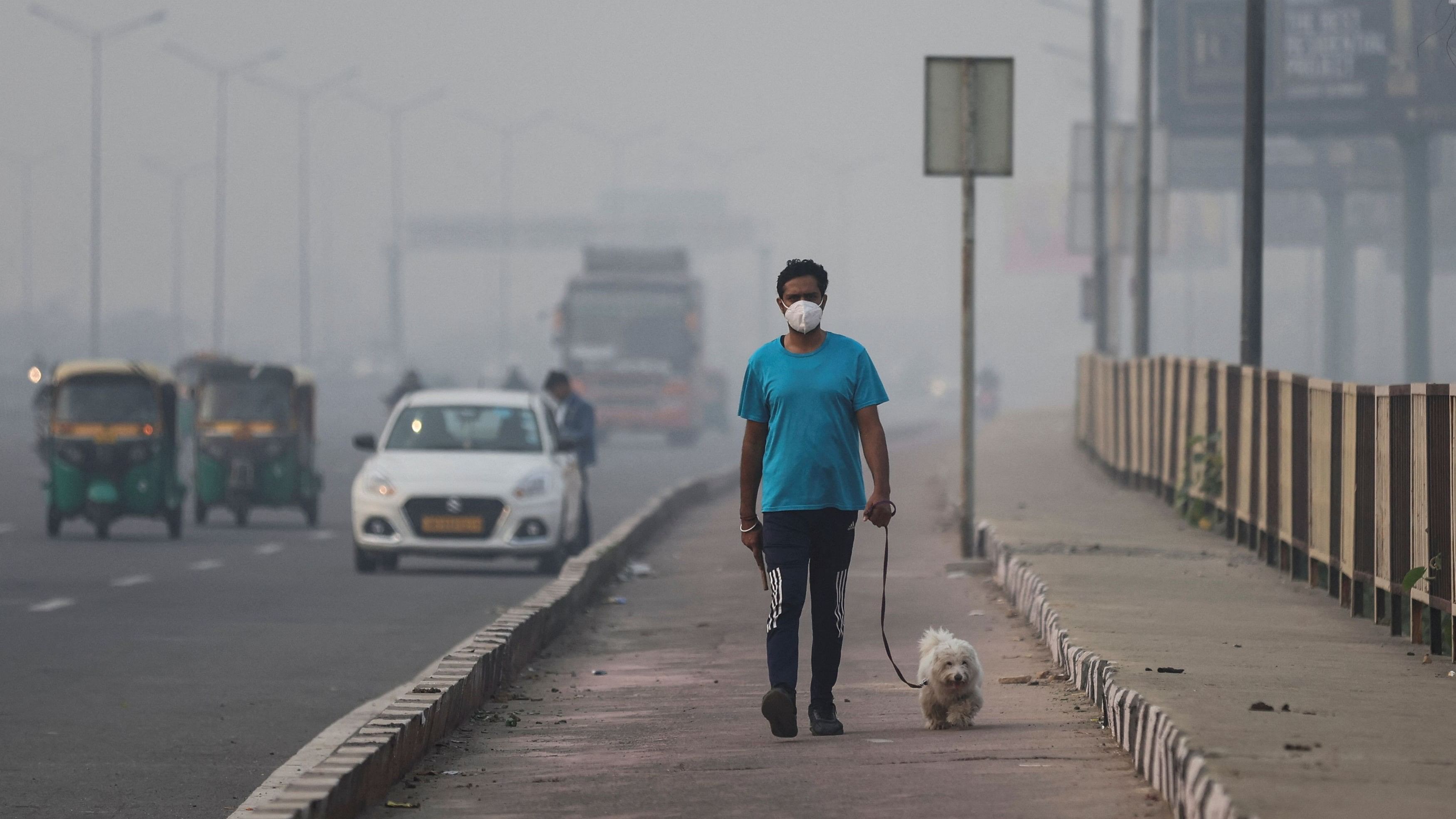 <div class="paragraphs"><p>A man wearing face mask walks with his dog on a footpath amidst the morning smog in New Delhi.&nbsp;</p></div>