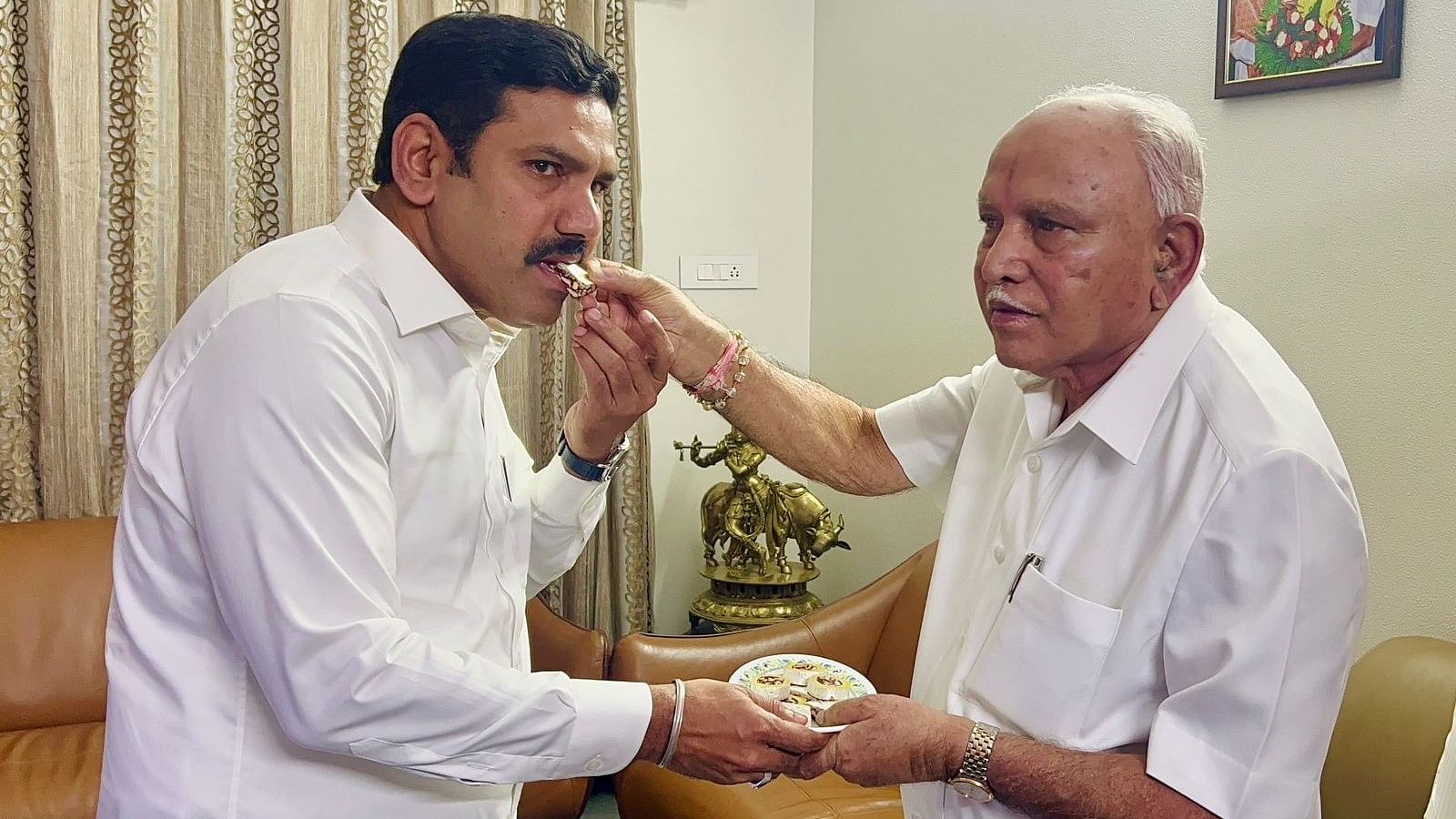 Former chief minister B S Yediyurappa offers sweet to his son B Y Vijayendra, on latter's appointment as the BJP's Karnataka president, in Bengaluru on Friday. 