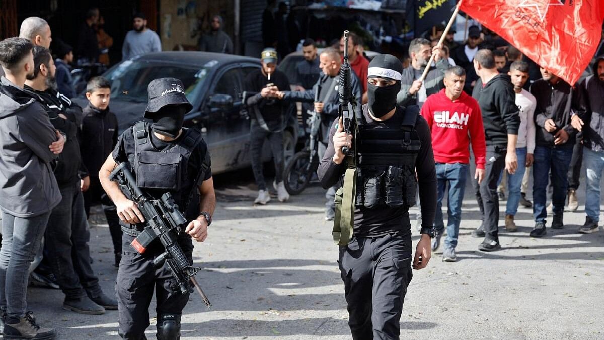 <div class="paragraphs"><p>Armed men walk as the bodies of Palestinians (not pictured), who were killed during an Israeli raid, are carried through the streets in Jenin, in the Israeli-occupied West Bank.&nbsp;</p></div>