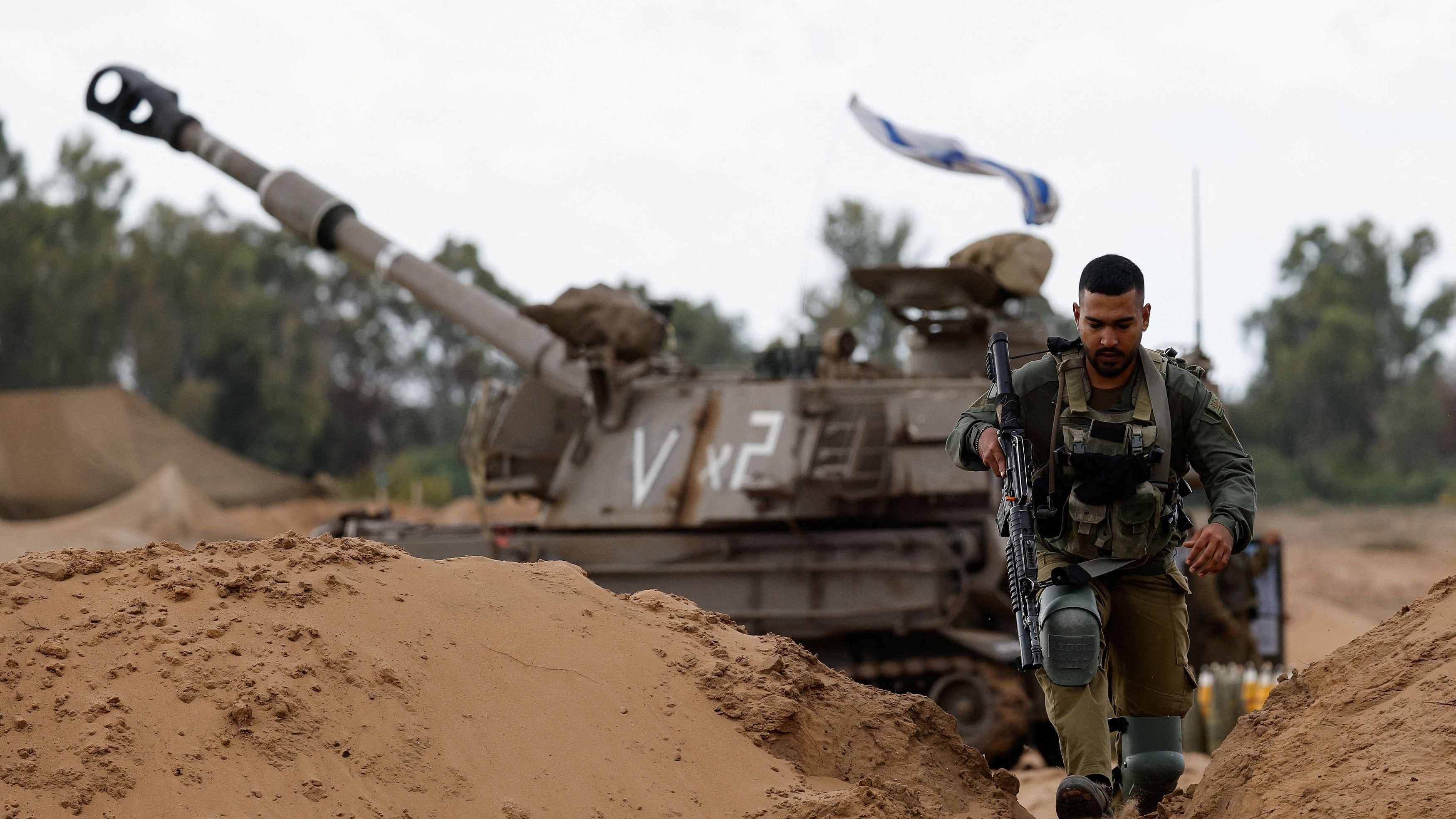 <div class="paragraphs"><p>An Israeli soldier walks by a mobile artillery unit, amid the ongoing conflict between Israel and the Palestinian Islamist group Hamas, near the northern Gaza border, in southern Israel.</p></div>