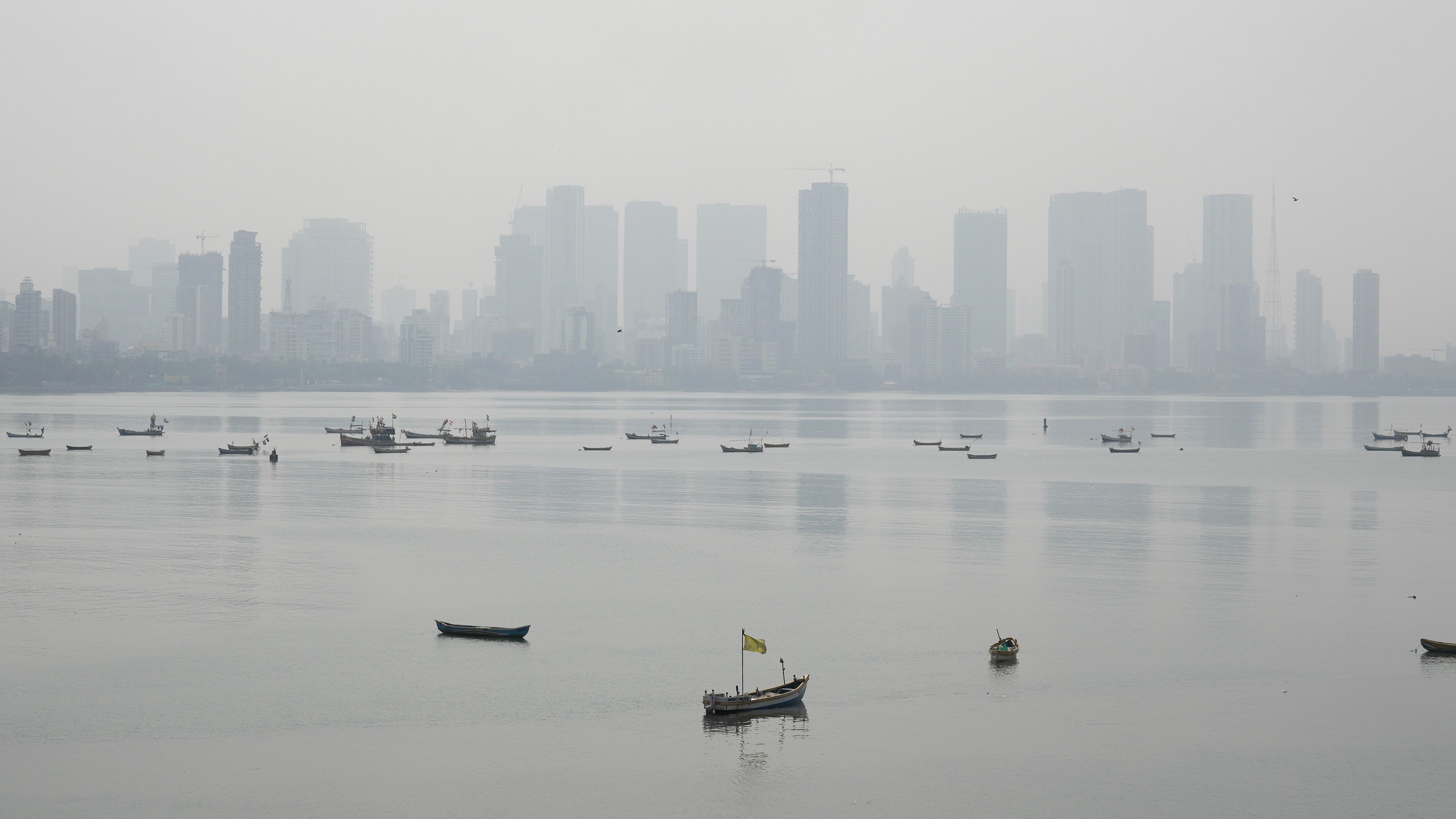 <div class="paragraphs"><p>Fishing boats are seen in the backdrop of the city skyline covered by smog, in Mumbai.</p></div>