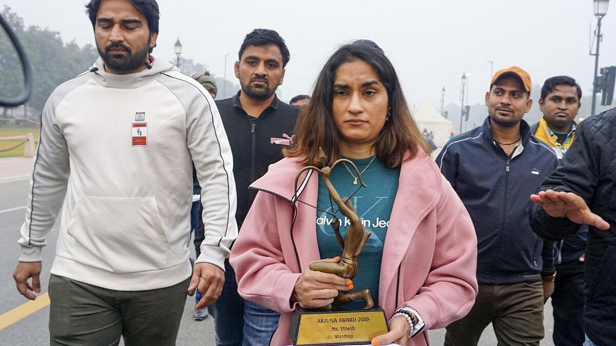 <div class="paragraphs"><p>Wrestler Vinesh Phogat walks with her Arjuna and Khel Ratna Awards, India's highest national sports awards, before leaving them on a pavement near the prime minister's office as a mark of protest, in New Delhi</p></div>