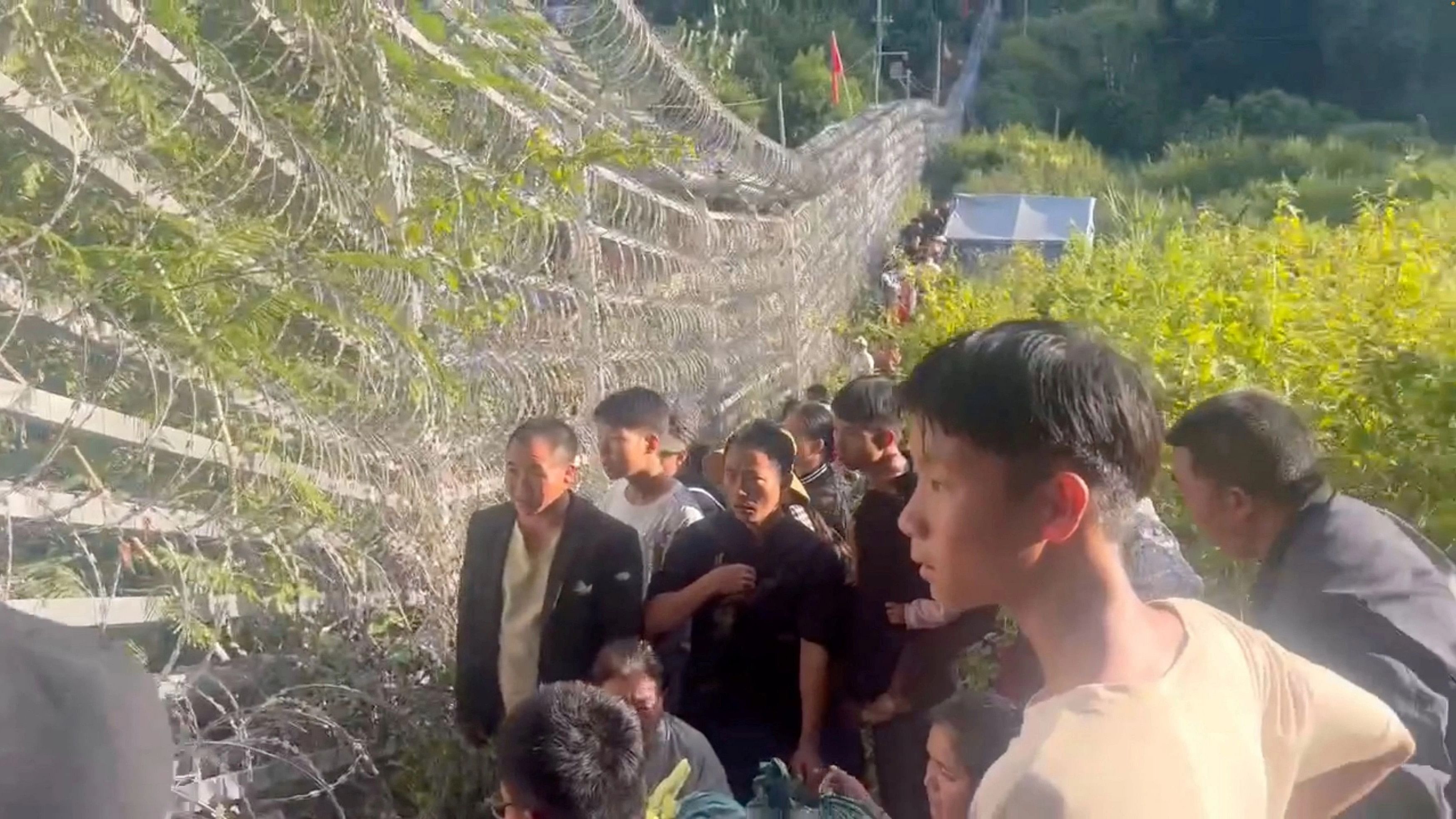 <div class="paragraphs"><p>People on the Myanmar side of the Myanmar-China border stand near the fence in this screen grab taken from a social media video filmed from Laukkang.</p></div>