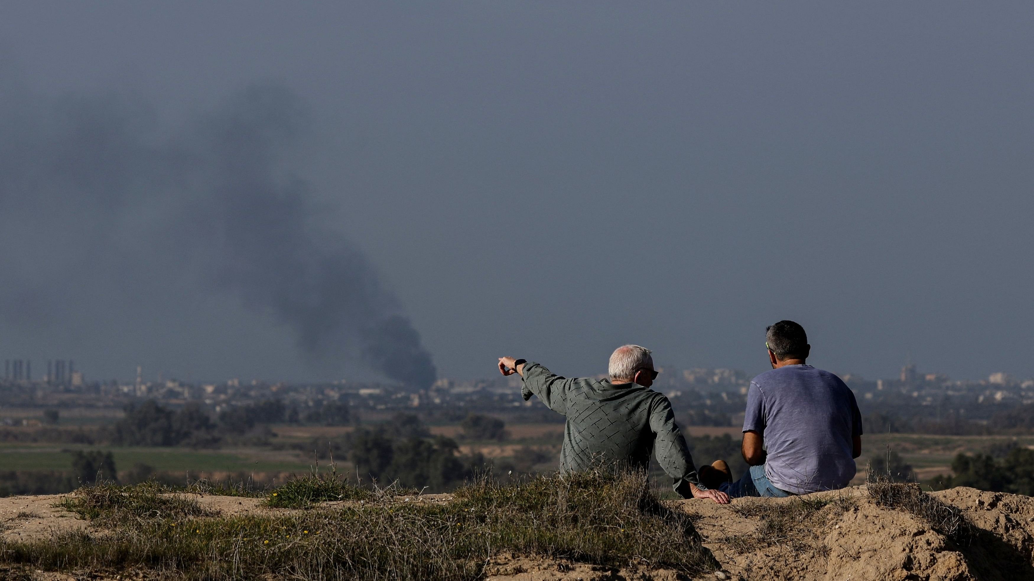 <div class="paragraphs"><p>Men sit on a hillside as the smoke rises from the Gaza Strip near the Israel-Gaza border.</p></div><div class="paragraphs"><p><br></p></div>