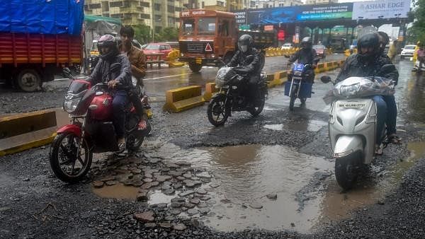 <div class="paragraphs"><p>Commuters ride past pot-holes filled road after heavy rainfall, in Mumbai.</p></div>