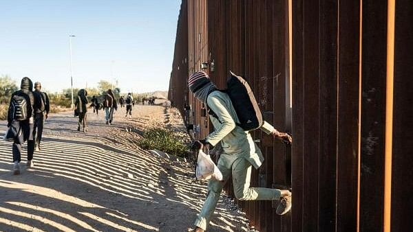 <div class="paragraphs"><p>Migrants from various countries in Africa and Latin America cross the border wall through a gap into the US from Mexico.</p></div>