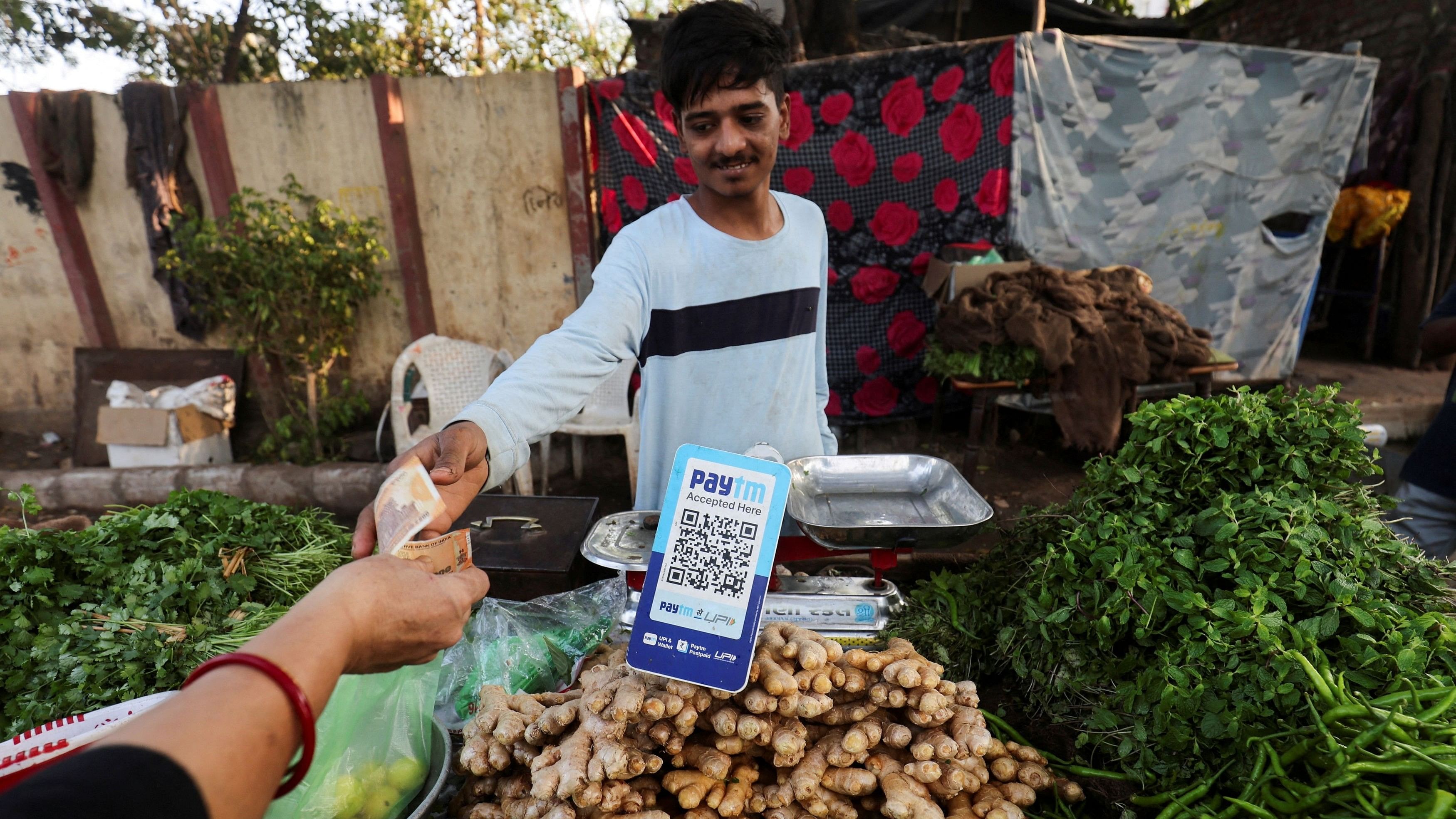 <div class="paragraphs"><p>A customer pays cash to buy vegetables next to a QR code of Paytm, a digital payments firm, on display at a roadside market in Ahmedabad, India, February 5, 2024.</p></div>
