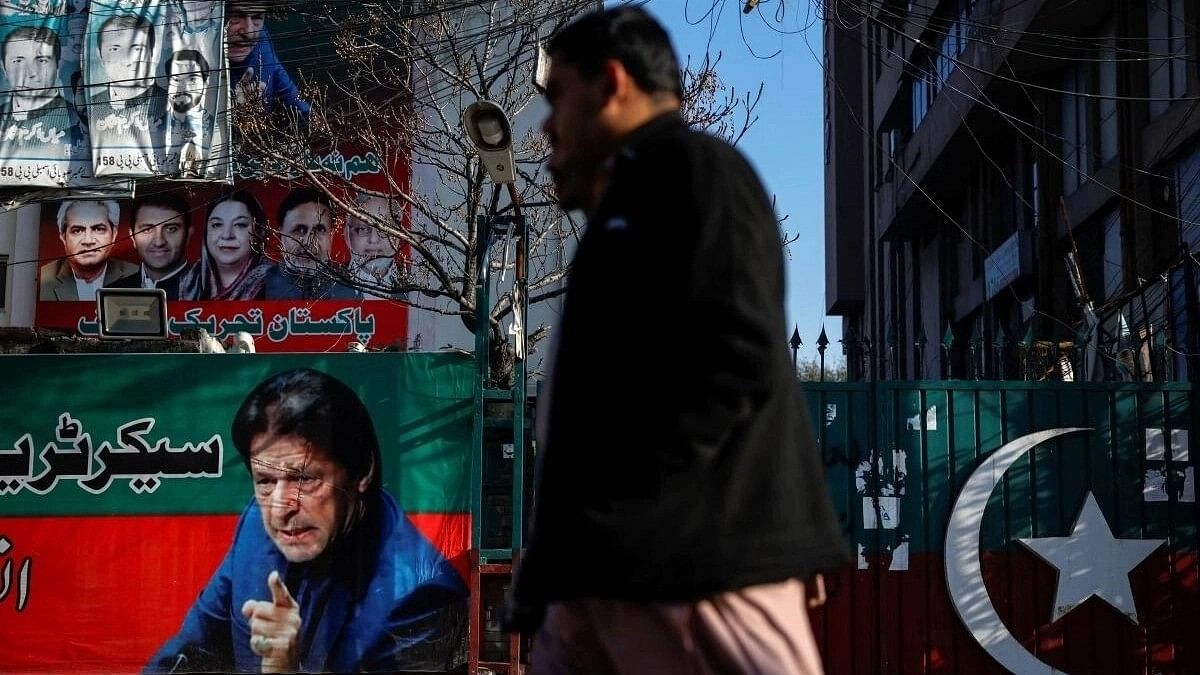 <div class="paragraphs"><p>People walk past a banner with a picture of the former Prime Minister Imran Khan outside the party office of Pakistan Tehreek-e-Insaf (PTI).</p></div>