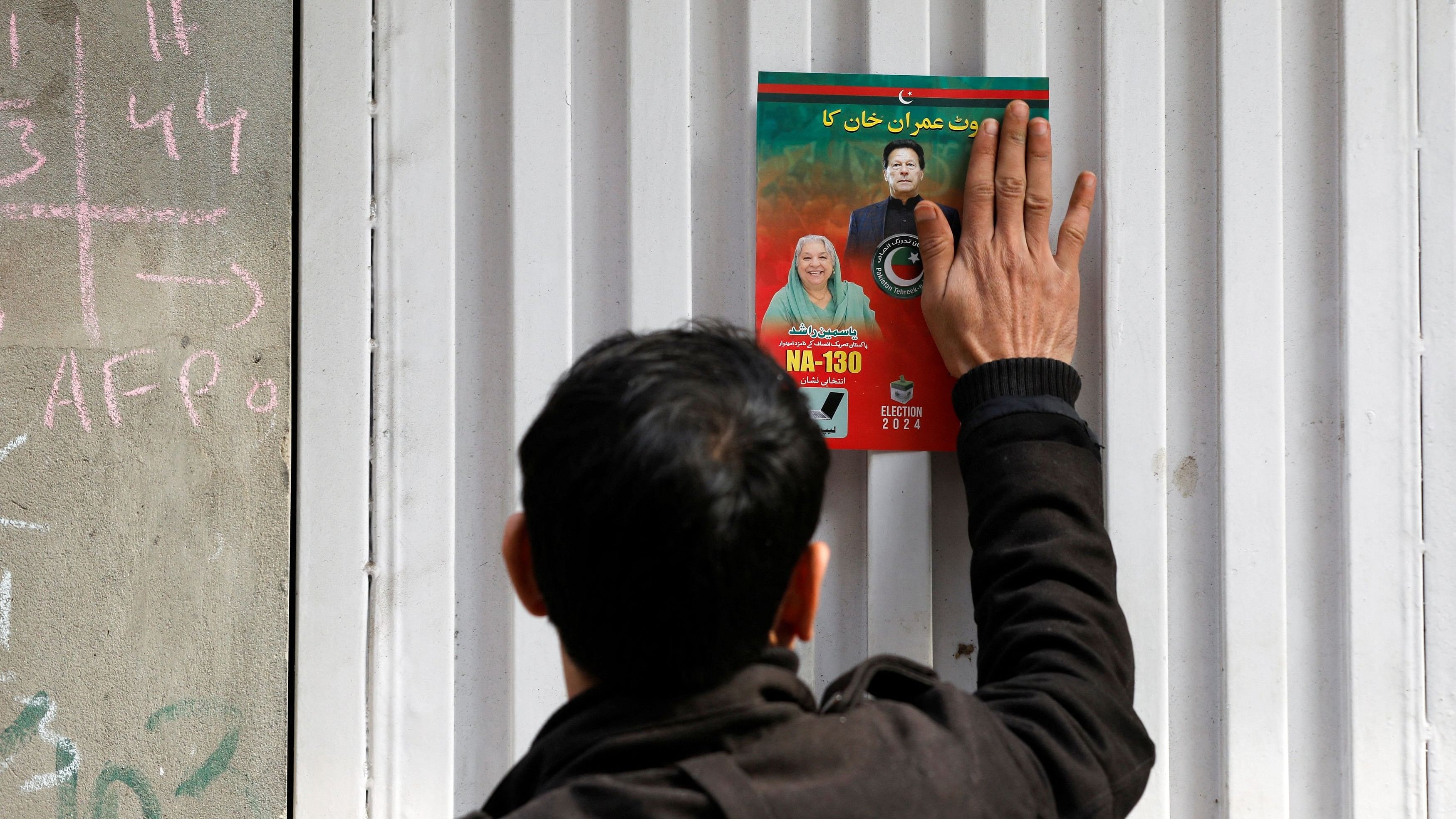 <div class="paragraphs"><p>A supporter of former Prime Minister Imran Khan pastes a poster of the candidate on the entrance of a house during a door-to-door campaign, ahead of the general elections in Lahore.</p></div>