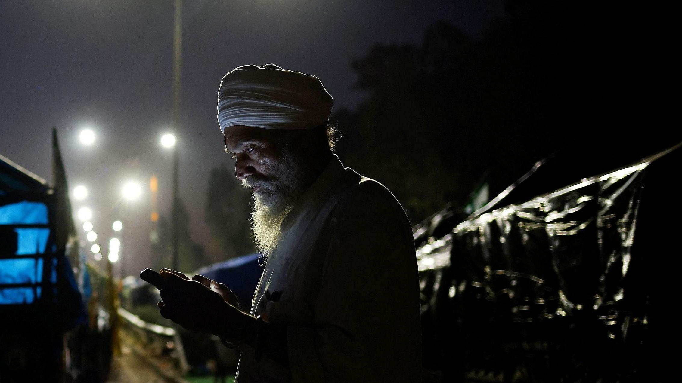 <div class="paragraphs"><p>A farmer looks at his phone as he stands next to his tractor trolley as farmers march towards New Delhi to push for better crop prices promised to them in 2021, at Shambhu Barrier, the border between Punjab and Haryana states.</p></div>