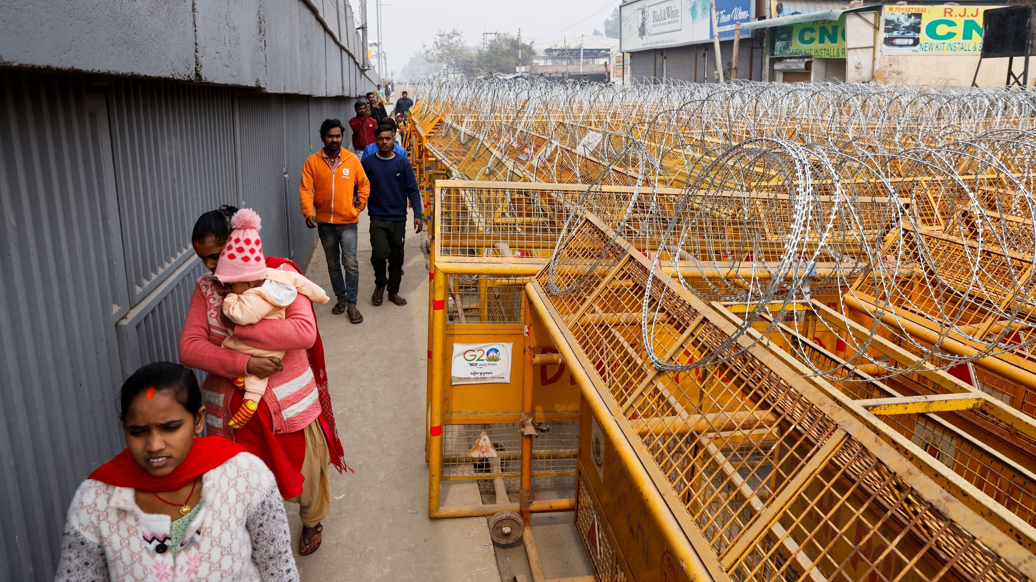 <div class="paragraphs"><p>People walk by barricades as police officers and workers erect them on a national highway to stop farmers, who are marching towards New Delhi to press for the better crop prices promised to them in 2021, at the Singhu border in New Delhi, India, February 13, 2024. </p></div>