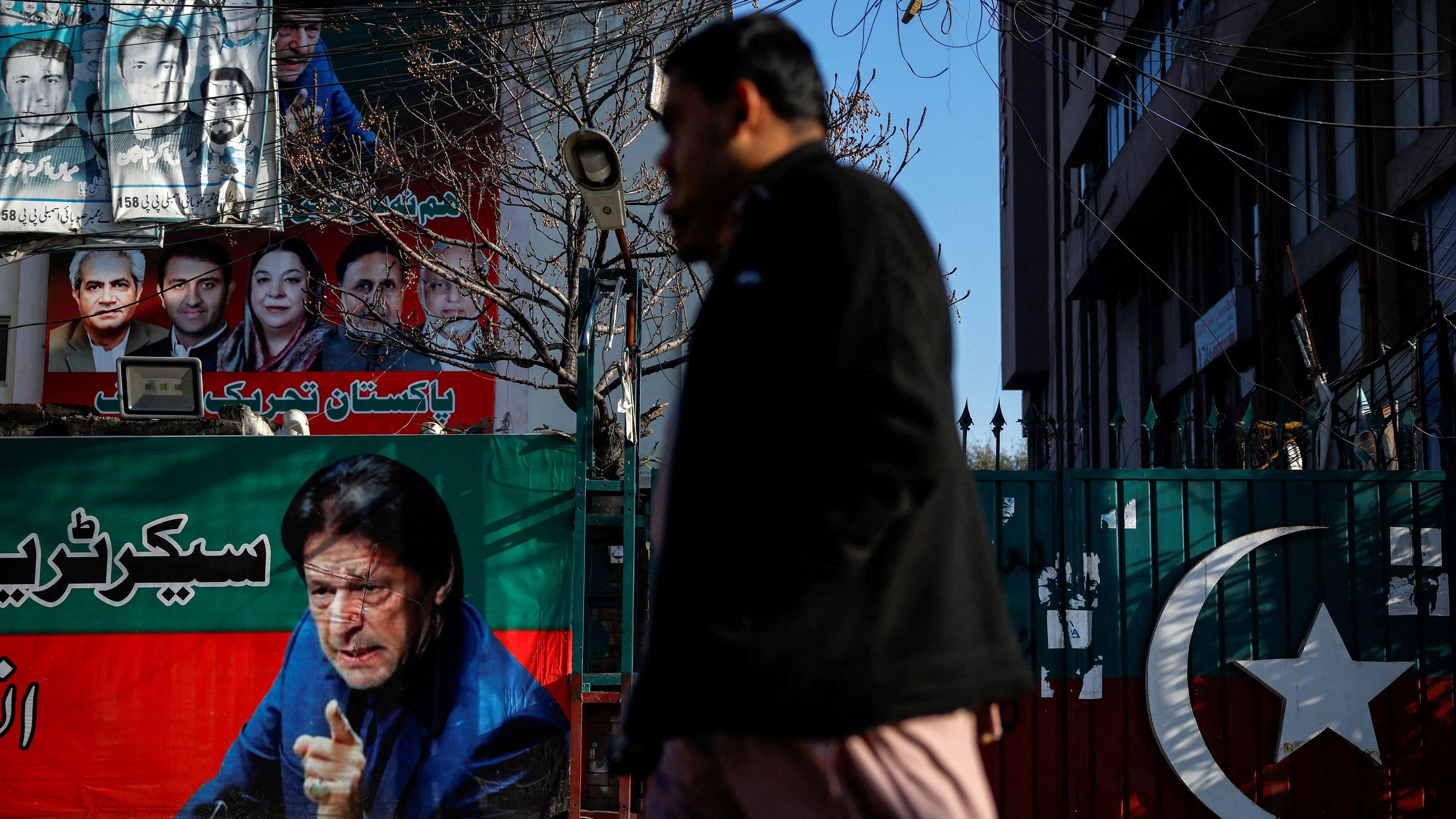 <div class="paragraphs"><p>People walk past a banner with a picture of the former Prime Minister Imran Khan outside the party office of PTI, a day after the general election, in Lahore, Pakistan, Feb 9, 2024.</p></div>