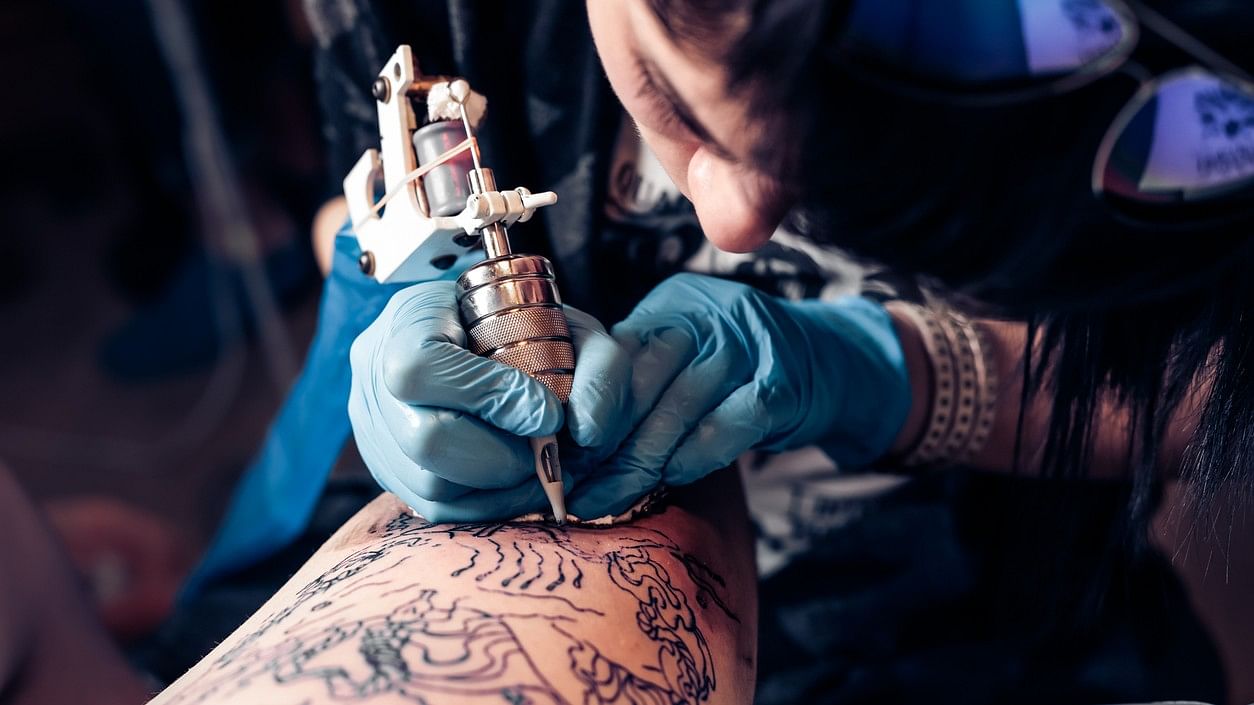 Professional tattoo artist makes a tattoo on a woman's leg. Process.  Close-up of a tattoo machine. Stock Photo by StudioPeace