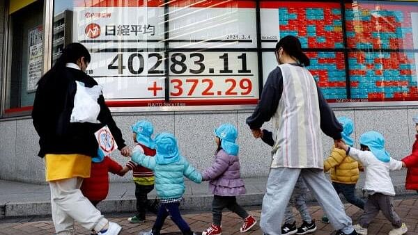 <div class="paragraphs"><p>Children and their teachers walk past an electronic screen displaying Japan's Nikkei share average outside a brokerage in Tokyo.</p></div>