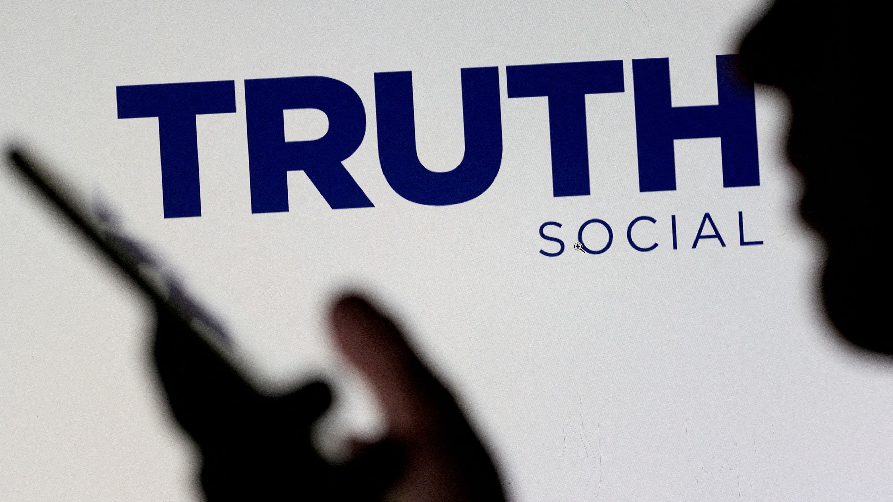 <div class="paragraphs"><p>The Truth social network logo is seen displayed behind a woman holding a smartphone.</p></div>