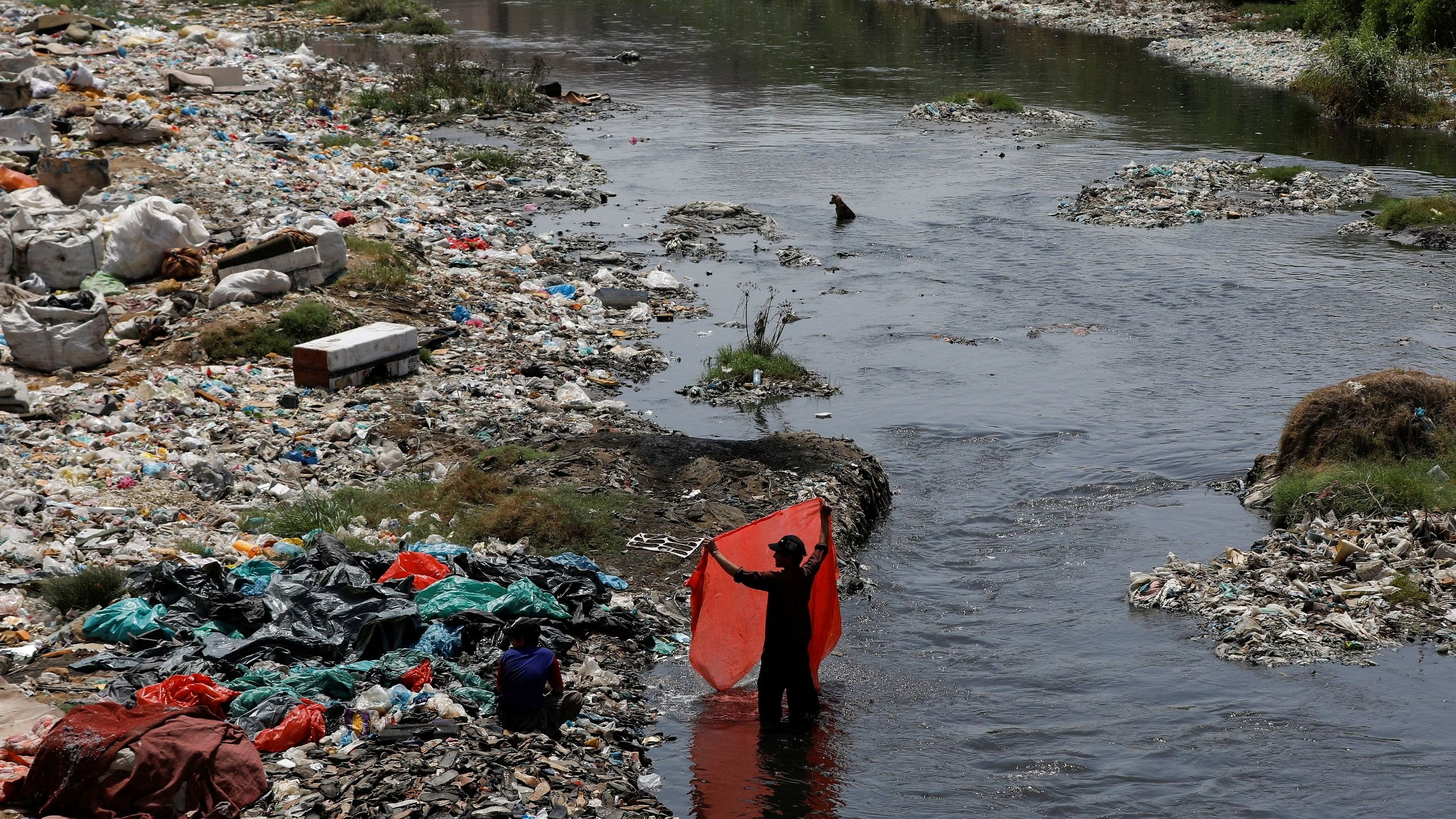 <div class="paragraphs"><p> A man washes waste plastic sheets, collected for recycling, in the polluted waters.</p></div>