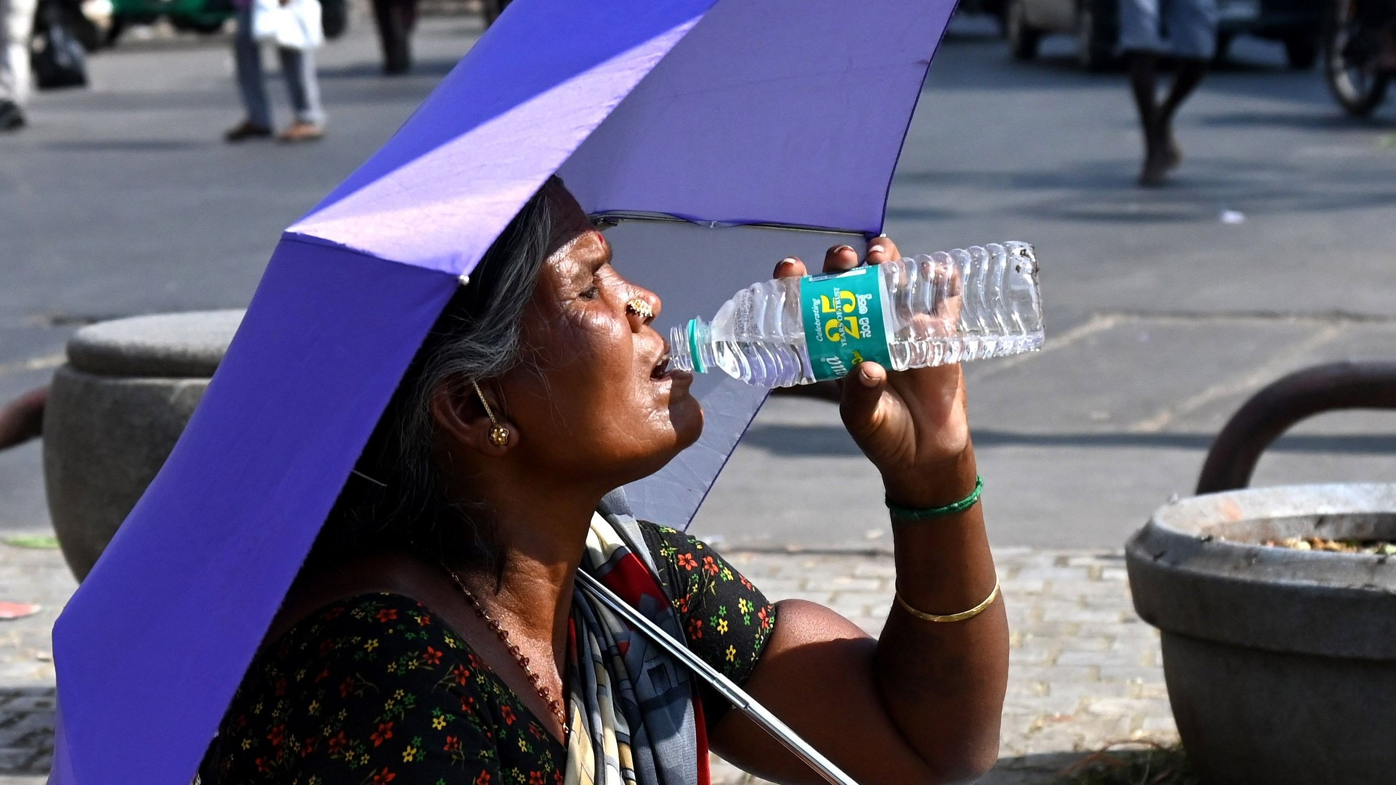 <div class="paragraphs"><p>In the blistering heat, a street vendor finds respite under her trusty umbrella, sipping from a bottle of water to ease her parched throat. </p></div>