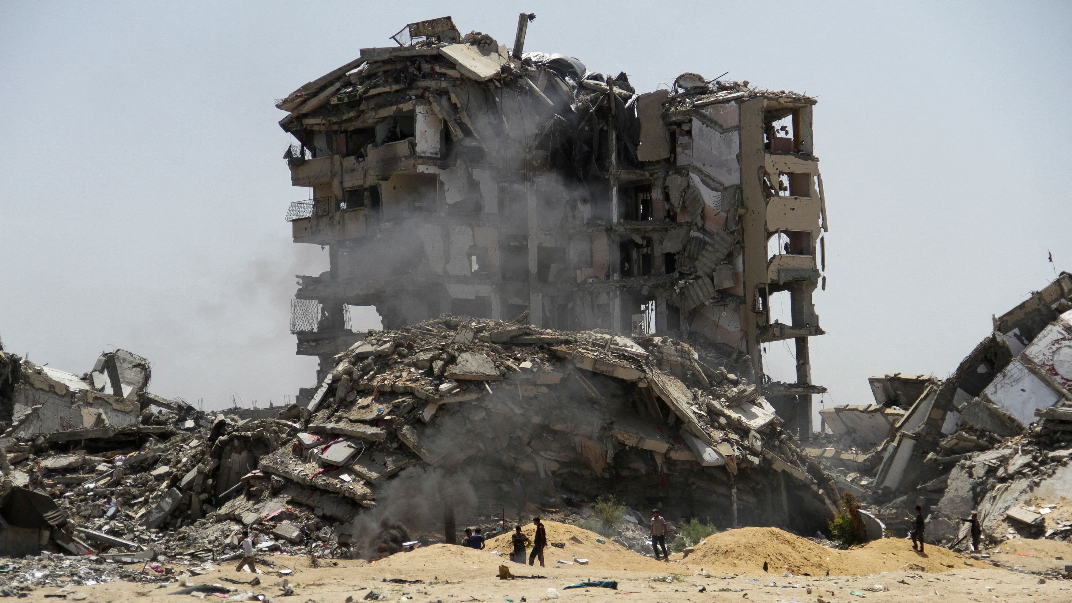 <div class="paragraphs"><p>Palestinians walk past the rubble of residential buildings destroyed by Israeli strikes.</p></div>