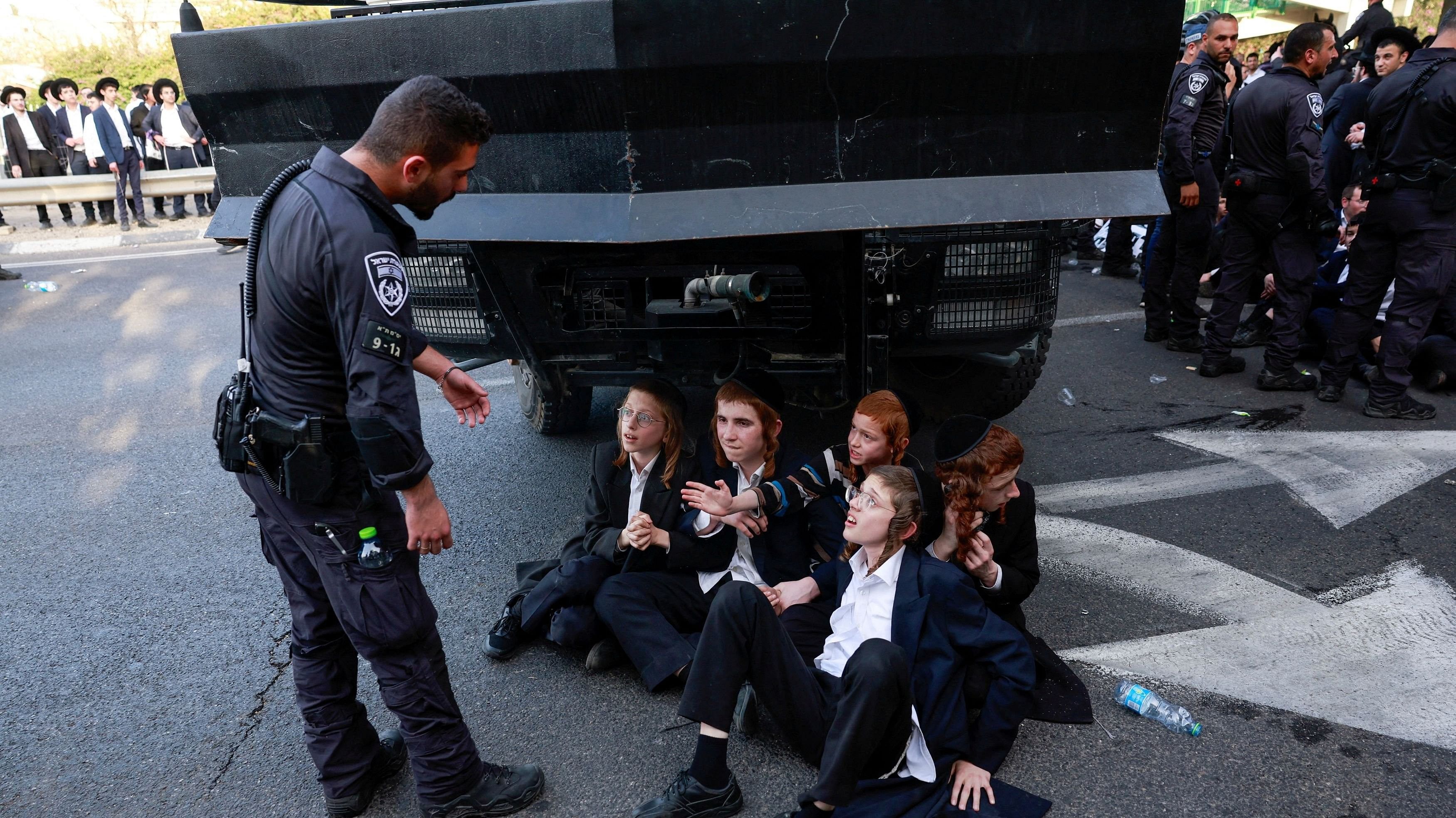 <div class="paragraphs"><p>Ultra-Orthodox Jewish demonstrators sit on the street next to a police officer, as they attempt to block a main road, in protest against attempts to change government policy that grants ultra-Orthodox Jews exemptions from military conscription, at the entrance to Bnei Brak, Israel, April 1, 2024. </p></div>