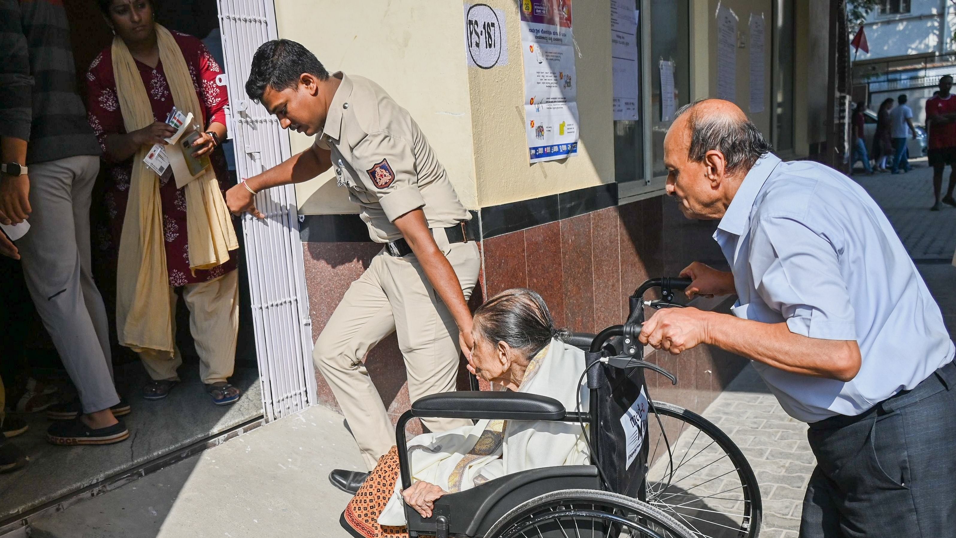<div class="paragraphs"><p>A policeman helps a wheelchair-bound senior citizen into a polling booth in Lakkasandra on Friday.&nbsp;</p></div>