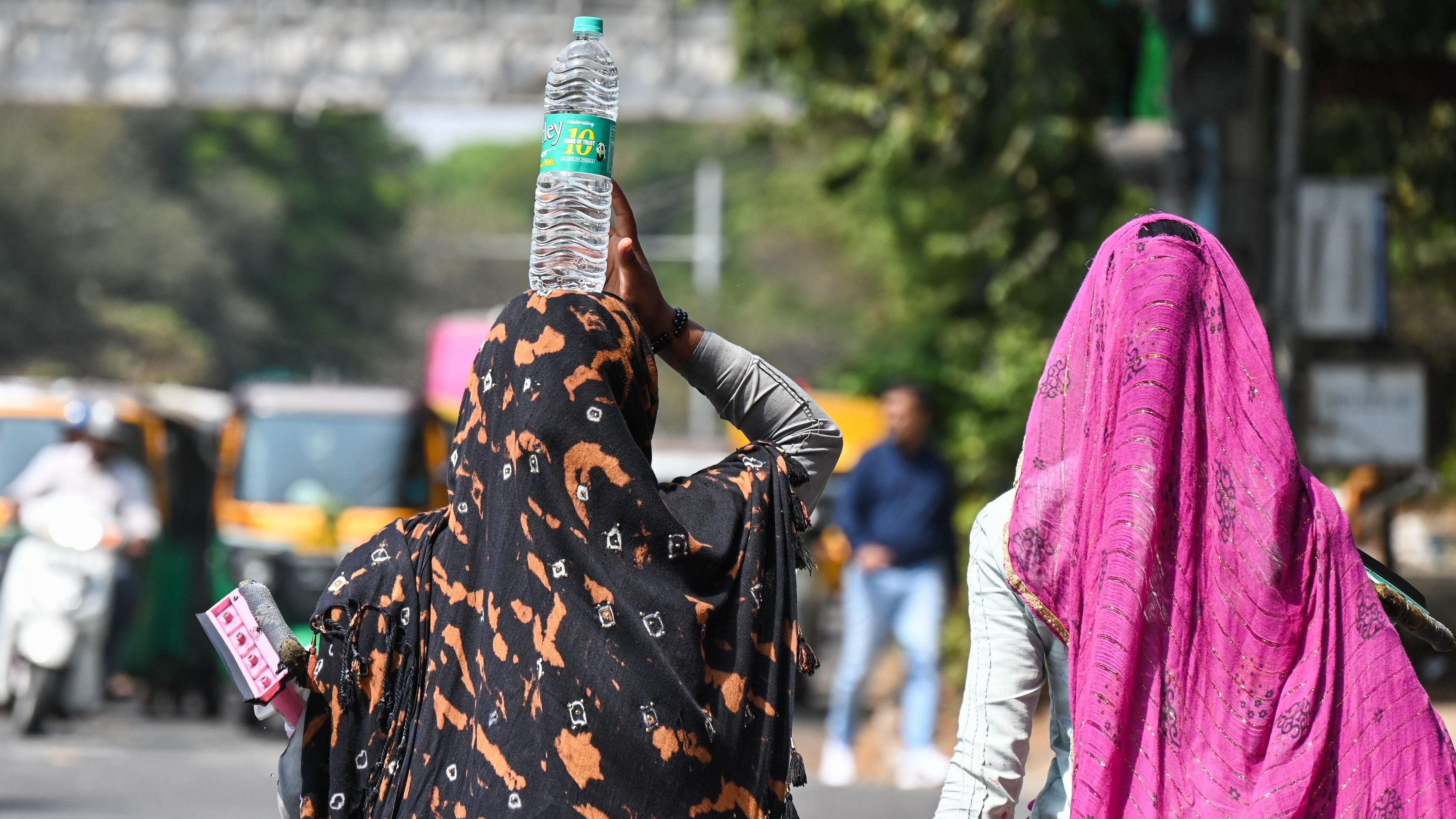 A woman carries a water bottle on her head to beat the heat in Bengaluru. DH Photo file photo