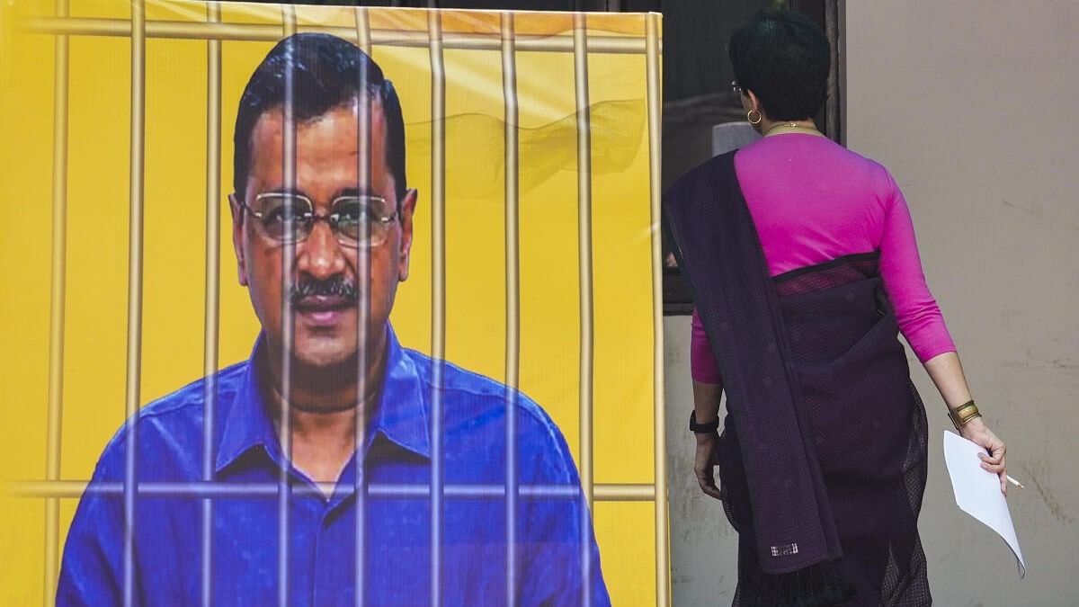 <div class="paragraphs"><p>AAP's Atishi walks past a banner showing Delhi CM Arvind Kejriwal behind bars.</p></div>