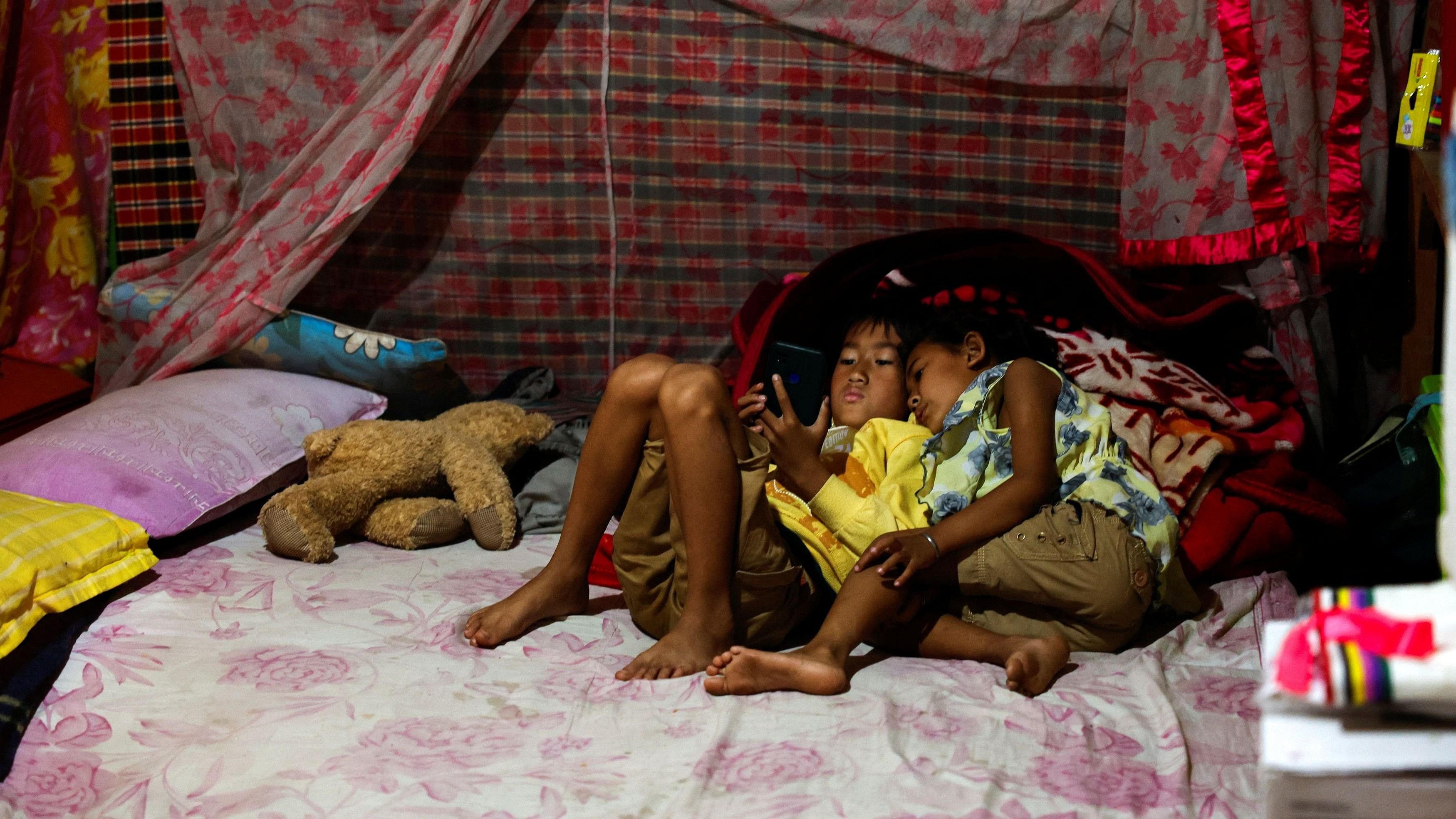 <div class="paragraphs"><p>Francis Keisham's children, Nganba Keisham, 8 and Thasana Keisham, 5, look at a mobile phone inside their temporary home at a Meitei relief camp for displaced people in Imphal, Manipur, India, April 9, 2024.</p></div>